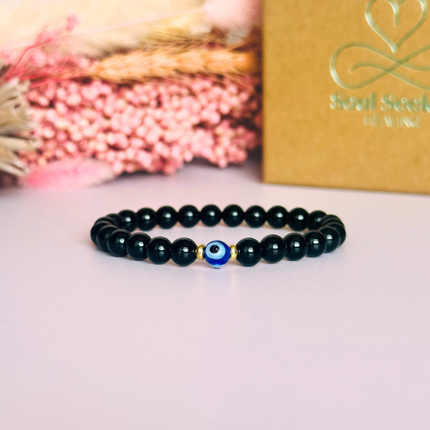Natural black tourmaline bracelet featuring ethically mined smooth 6mm round beads with a beautiful blue Turkish evil eye glass bead as the focal point. Finished with gold vermeil or sterling silver accent beads.