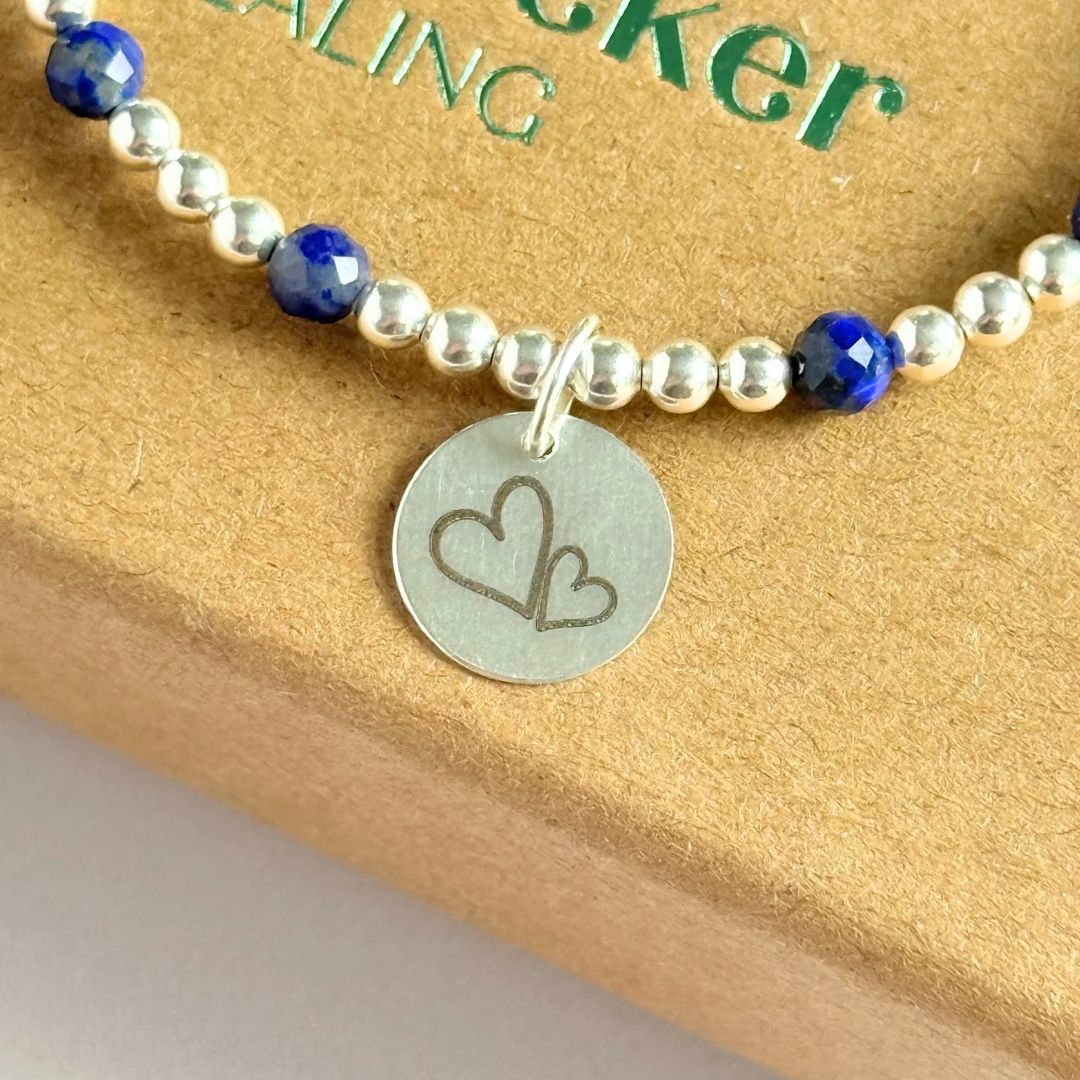Sterling silver bracelet features 4mm lapis lazuli faceted beads, separated by 3mm sterling silver round beads. Lapis lazuli is a September birthstone. The focal point is an 11mm sterling silver charm, engraved with a large and smaller heart design. This charm can be personalised on one side if required or feature the same graphic on both sides.