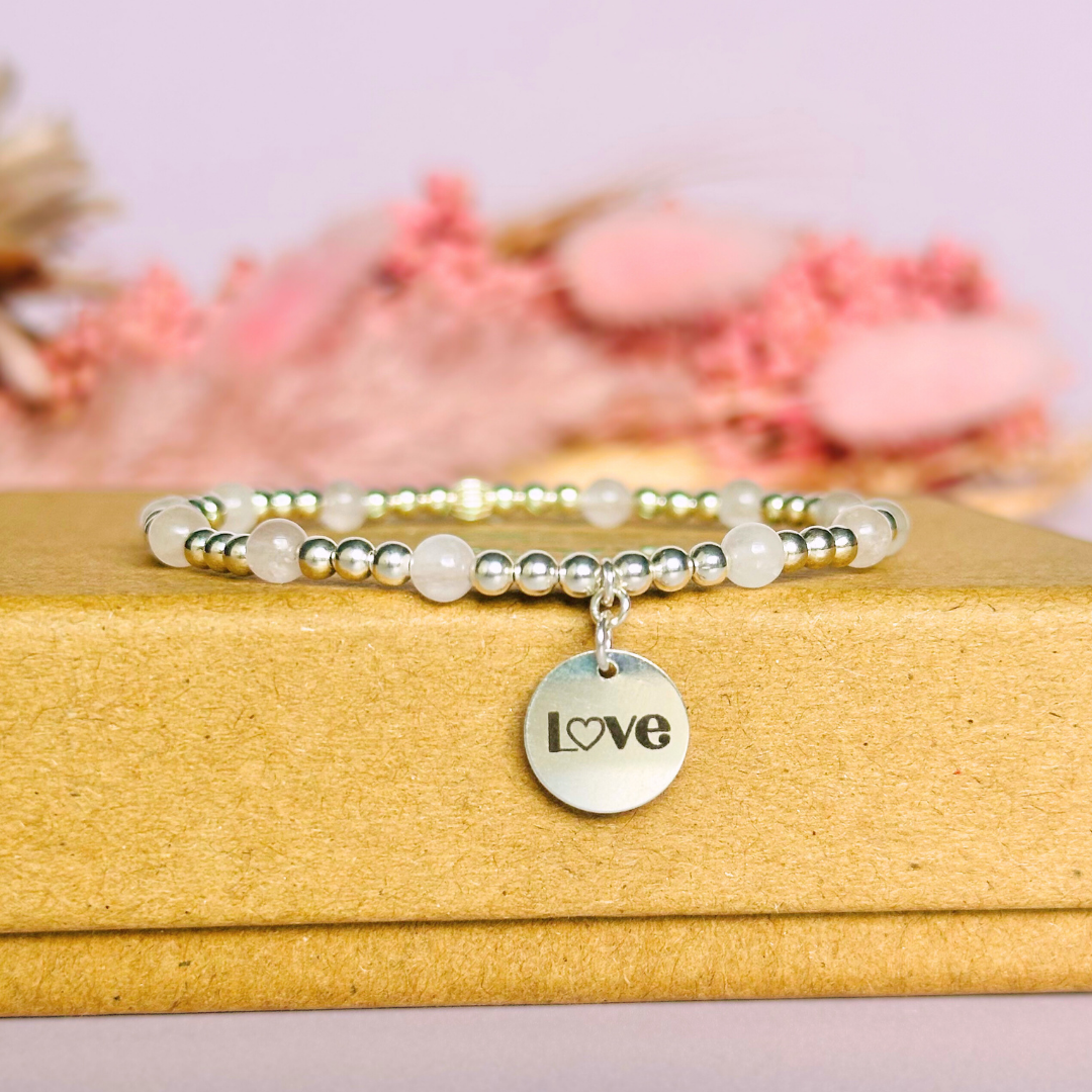 Sterling silver elasticated bracelet featuring 4mm round rose quartz beads, separated by 3mm sterling silver round ball beads. Featuring an 11mm sterling silver round disc charm engraved with the words love. One side of the charm can be personalised if required.