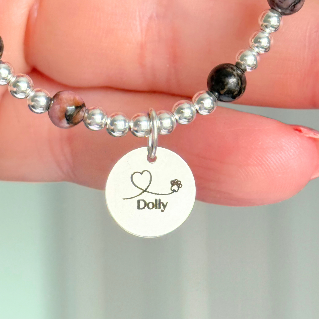 Sterling silver bracelet featuring ethically mined 4mm rhodonite crystal beads, separated by 3mm sterling silver beads. It features an 11mm sterling silver disc charm, which is engraved with a love heart and paw design, which can be personalised with your pet's name. The reverse of the charm says 'Forever in your heart x', although this side can also be personalised with your own words.