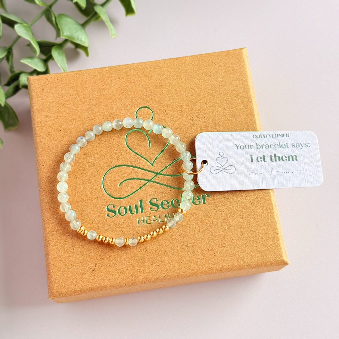 Elasticated labradorite crystal morse code bracelet that spells out the words ‘Let them’ in a combination of 4mm round labradorite beads, 4mm faceted labradorite beads and either sterling silver or gold vermeil 3mm round beads. The words start and end at the rondelle spacer beads.
