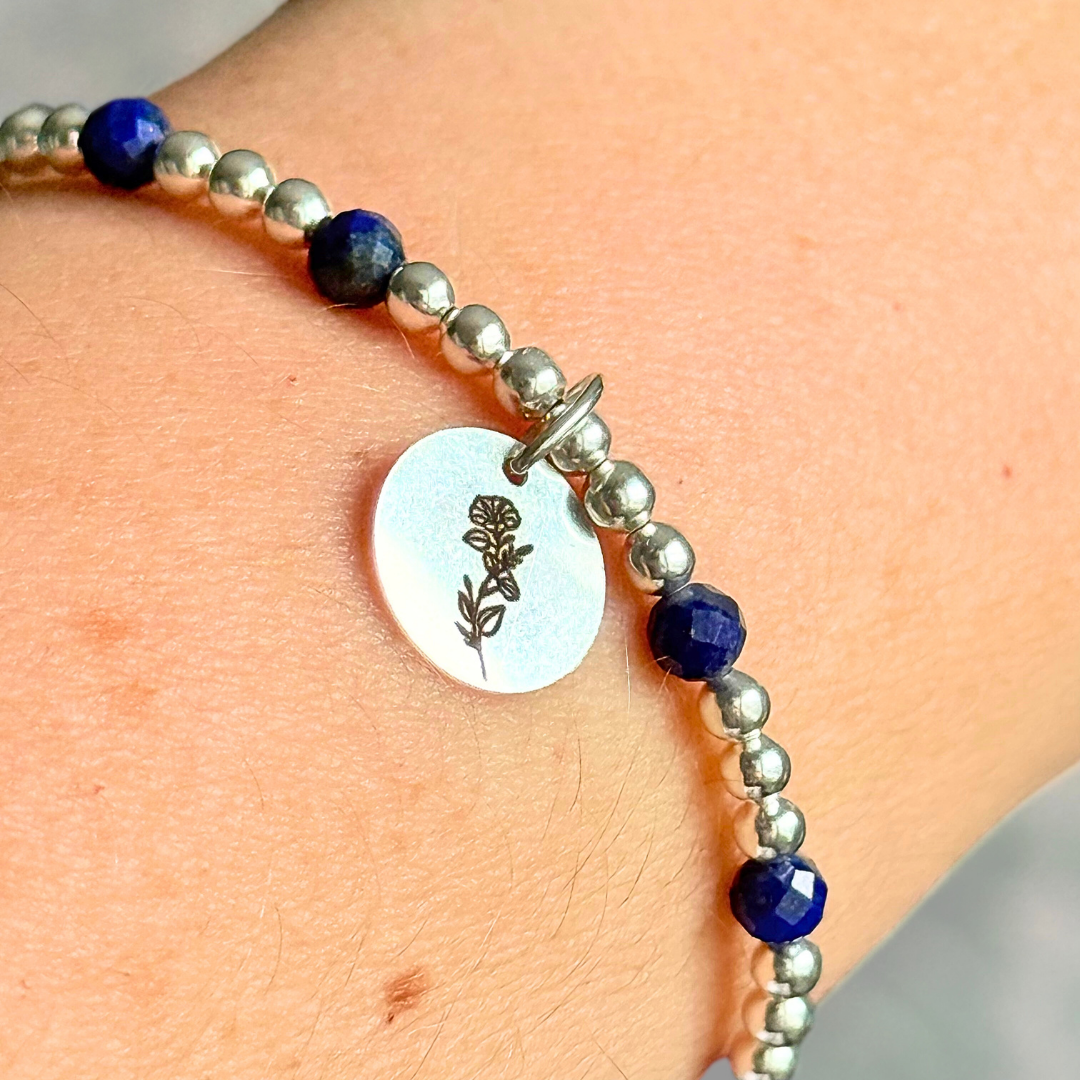 Sterling silver elasticated bracelet featuring 4mm faceted round lapis lazuli beads, separated by 3mm sterling silver round ball beads. Featuring an 11mm sterling silver round disc charm engraved with the September birth flower Morning Glory. One side of the charm can be personalised if required.