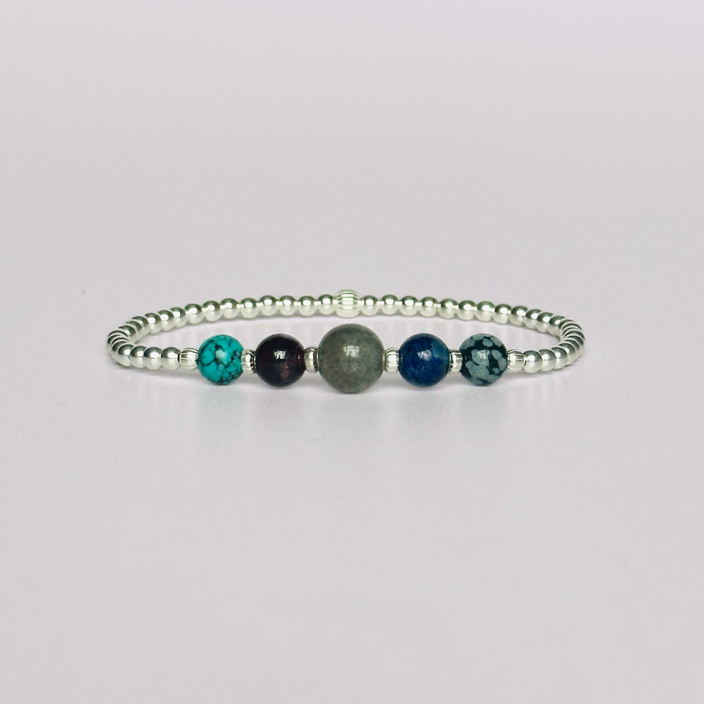 This sterling silver Sagittarius bracelet is made with a selection of five healing crystals all believed to resonate with the Sagittarius zodiac sign. The central bead is 8mm, the other four are 6mm. On an elasticated band of 3mm sterling silver beads with corrugated accent beads. Featuring garnet, labradorite, lapis lazuli, snowflake obsidian and turquoise.