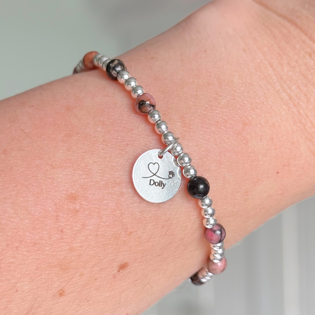 Sterling silver bracelet featuring ethically mined 4mm rhodonite crystal beads, separated by 3mm sterling silver beads. It features an 11mm sterling silver disc charm, which is engraved with a love heart and paw design, which can be personalised with your pet's name. The reverse of the charm says 'Forever in your heart x', although this side can also be personalised with your own words.