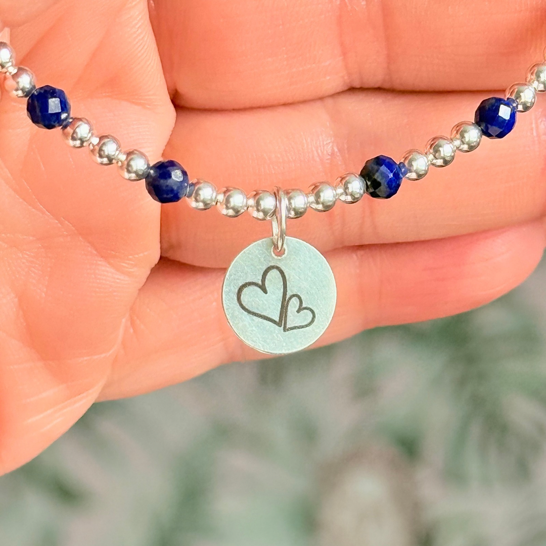 Sterling silver bracelet features 4mm lapis lazuli faceted beads, separated by 3mm sterling silver round beads. Lapis lazuli is a September birthstone. The focal point is an 11mm sterling silver charm, engraved with a large and smaller heart design. This charm can be personalised on one side if required or feature the same graphic on both sides.