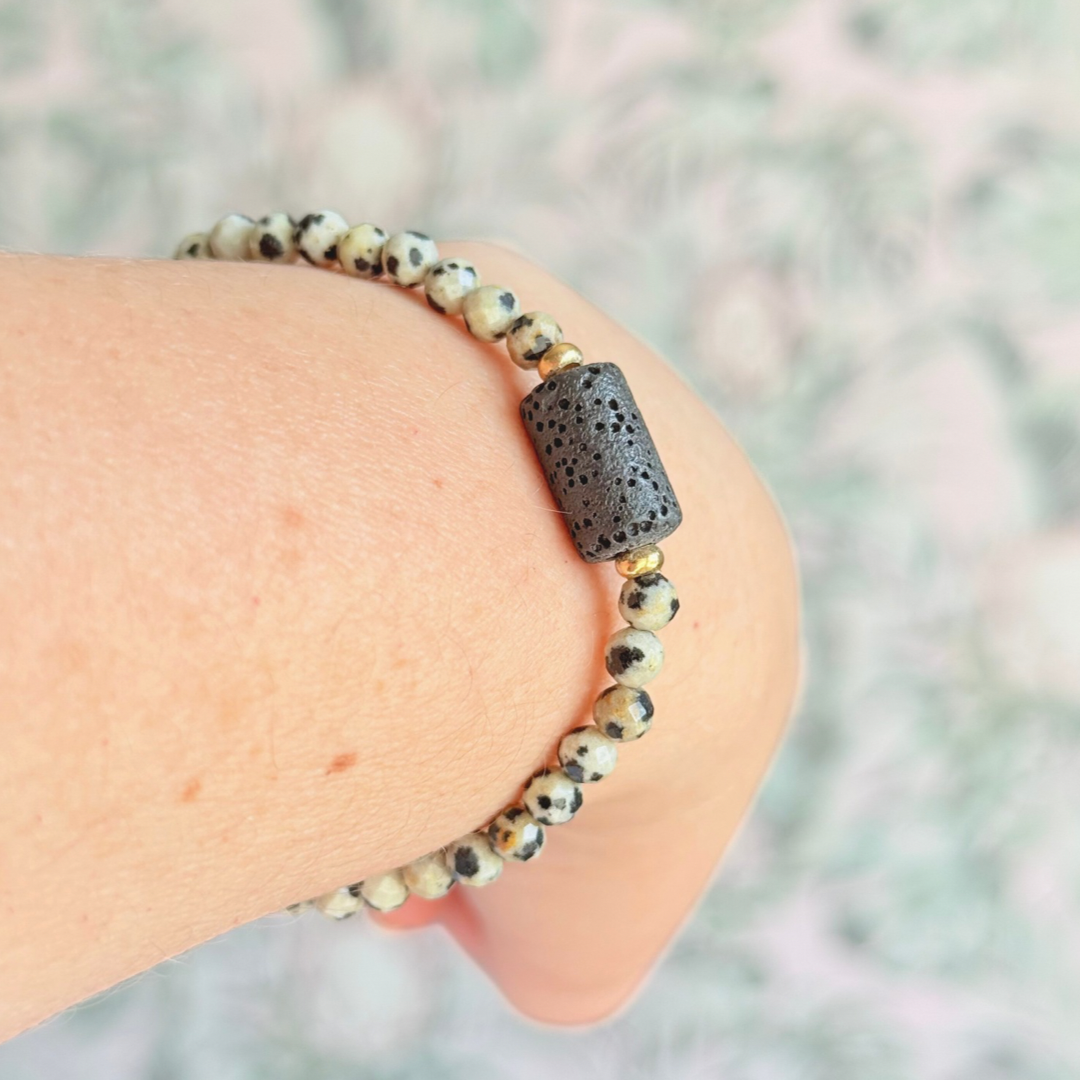 Essential oil diffuser bracelet featuring black lava rock tube bead on the band of 4mm faceted dalmatian jasper beads. Finished with your choice of sterling silver or gold vermeil accent beads.