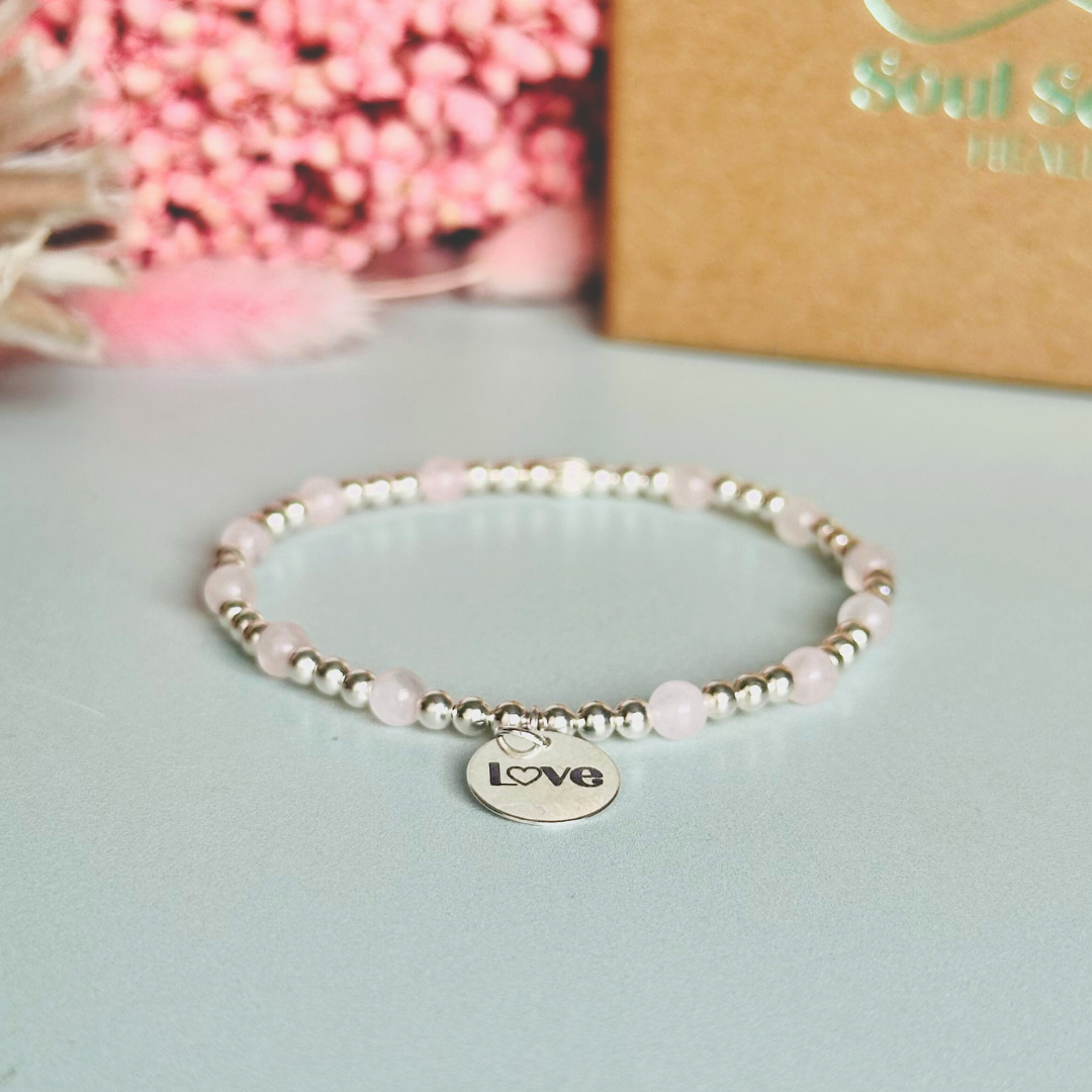 Sterling silver elasticated bracelet featuring 4mm round rose quartz beads, separated by 3mm sterling silver round ball beads. Featuring an 11mm sterling silver round disc charm engraved with the words love. One side of the charm can be personalised if required.