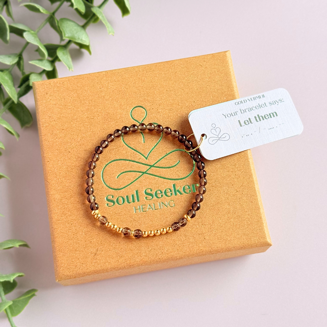 Elasticated smoky quartz crystal morse code bracelet that spells out the words ‘Let them’ in a combination of 4mm round smoky quartz beads, 4mm faceted smoky quartz beads and either sterling silver or gold vermeil 3mm round beads. The words start and end at the rondelle spacer beads.