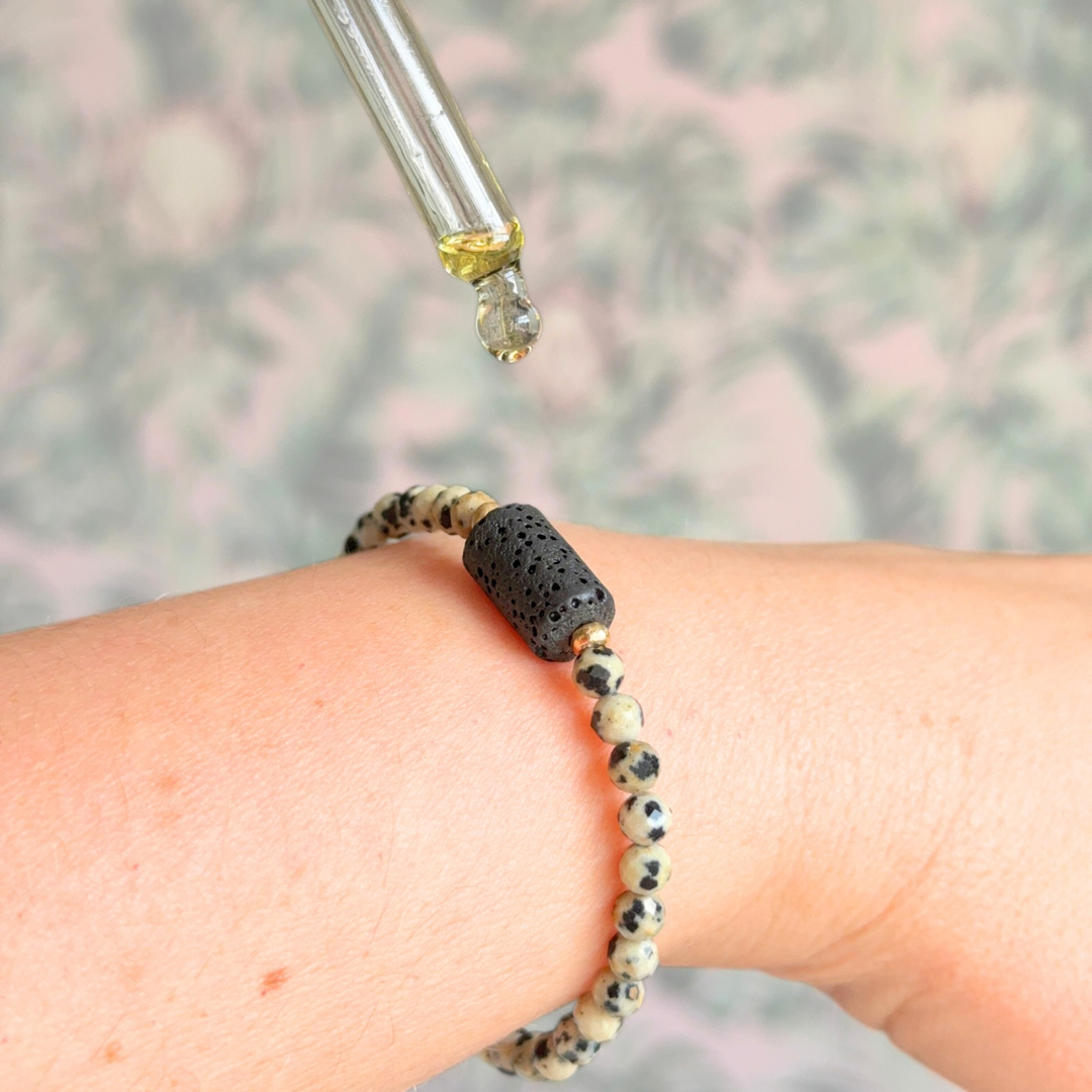 Essential oil diffuser bracelet featuring black lava rock tube bead on the band of 4mm faceted dalmatian jasper beads. Finished with your choice of sterling silver or gold vermeil accent beads.