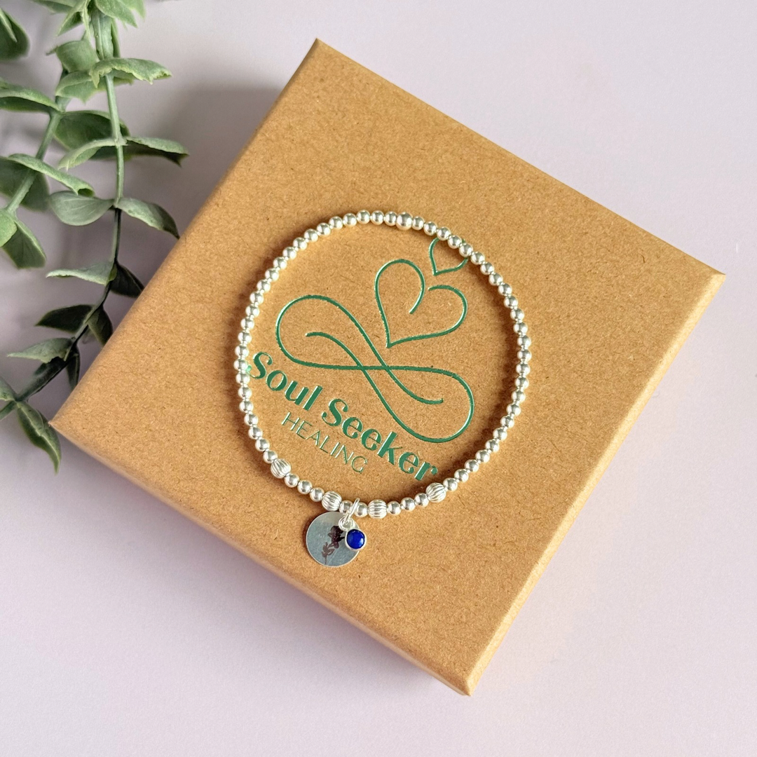 This sterling silver bracelet features a domed 4mm lapis lazuli cabochon charm, the birth stone for September, in a sterling silver setting. It features an 11mm sterling silver disc charm, which is engraved with the September birth flower, Morning Glory. This charm can be personalised on one side if required or feature the same flower graphic on both sides. The main band of the bracelet is made up of 3 mm sterling silver round ball beads with some corrugated accent beads.
