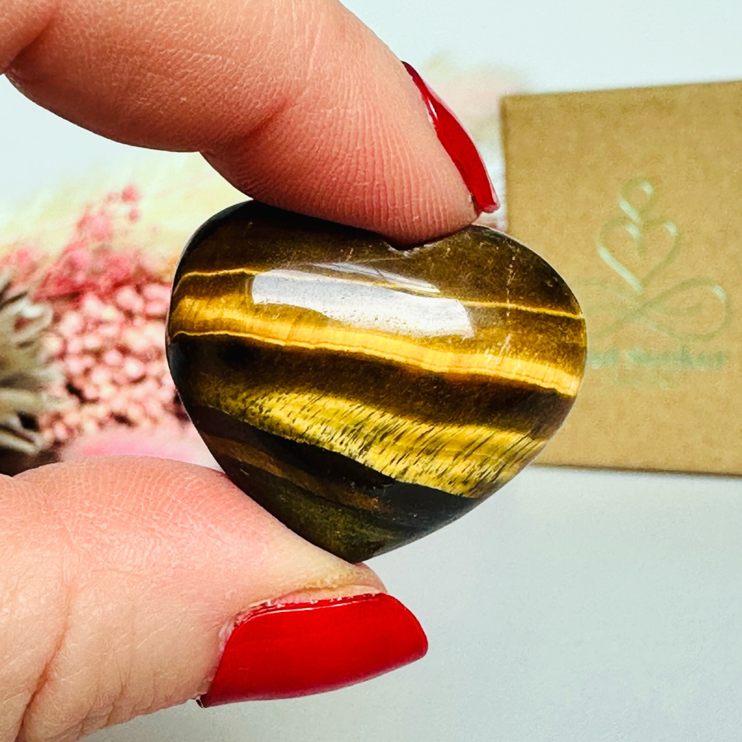 An ethically mined tigers eye heart, presented on an eco-friendly textured card with the words 'A stone of courage, protection and confidence. This heart shaped tigers eye crystal measures approximately 25mm x 25mm, making it an ideal size to carry with you wherever you go or to display in your sacred space. A cotton bag is included to keep it safe.