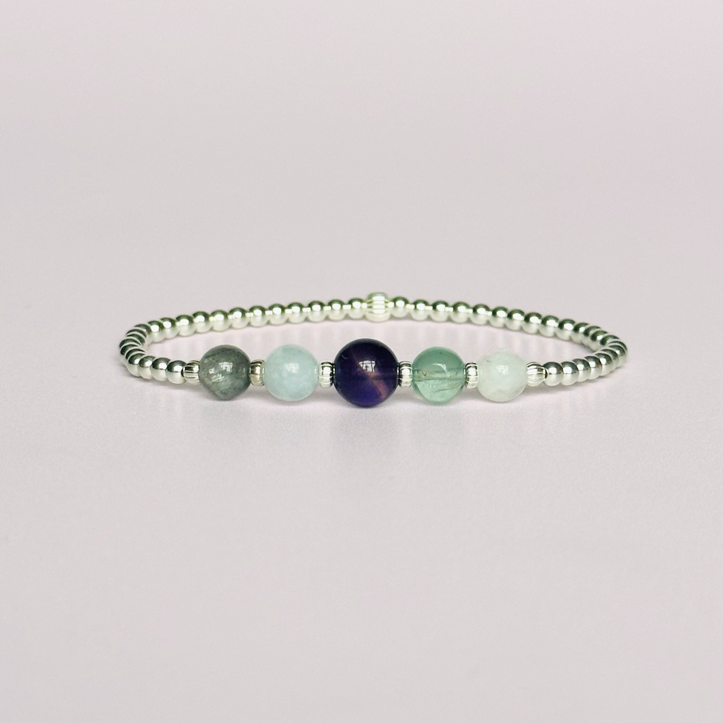 This sterling silver Aquarius bracelet is made with a selection of five healing crystals all believed to resonate with the Aquarius zodiac sign. The central bead is 8mm, the other four are 6mm. On an elasticated band of 3mm sterling silver beads with corrugated accent beads. Featuring labradorite, moonstone, fluorite, amethyst and aquamarine.
