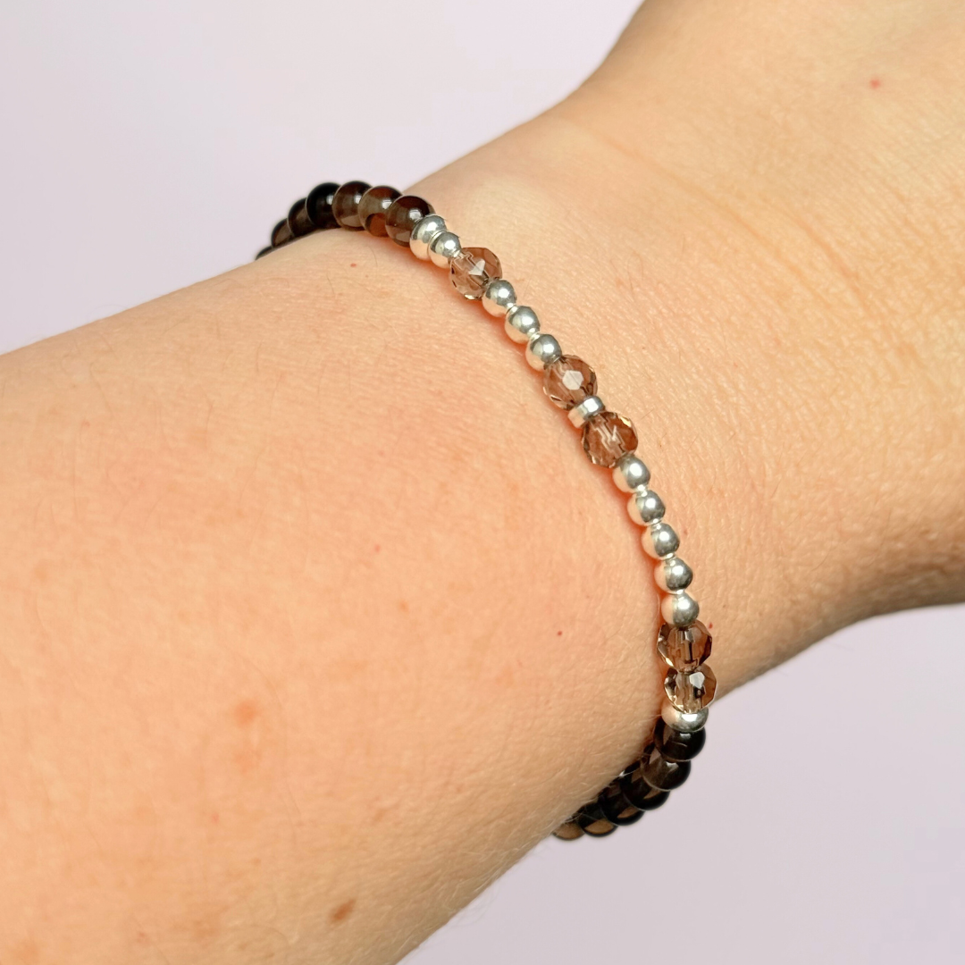 Elasticated smoky quartz crystal morse code bracelet that spells out the words ‘Let them’ in a combination of 4mm round smoky quartz beads, 4mm faceted smoky quartz beads and either sterling silver or gold vermeil 3mm round beads. The words start and end at the rondelle spacer beads.