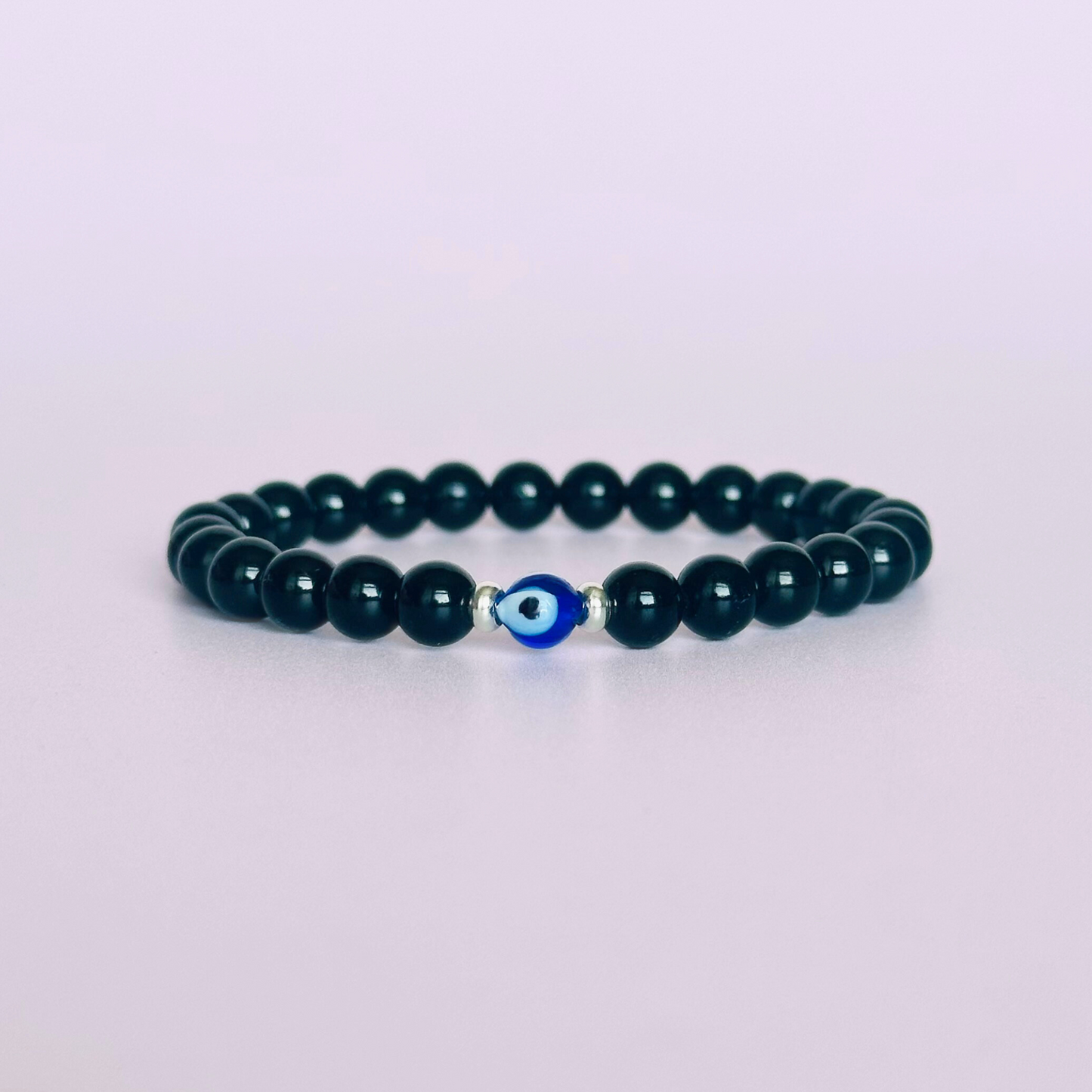 Natural black tourmaline bracelet featuring ethically mined smooth 6mm round beads with a beautiful blue Turkish evil eye glass bead as the focal point. Finished with gold vermeil or sterling silver accent beads.