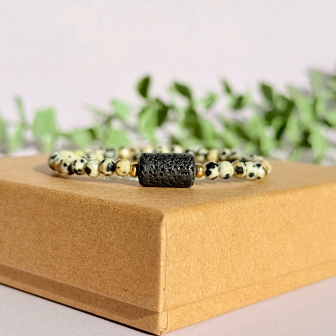 Essential oil diffuser bracelet featuring black lava rock tube bead on the band of 4mm faceted dalmatian jasper beads. Finished with your choice of sterling silver or gold vermeil accent beads.