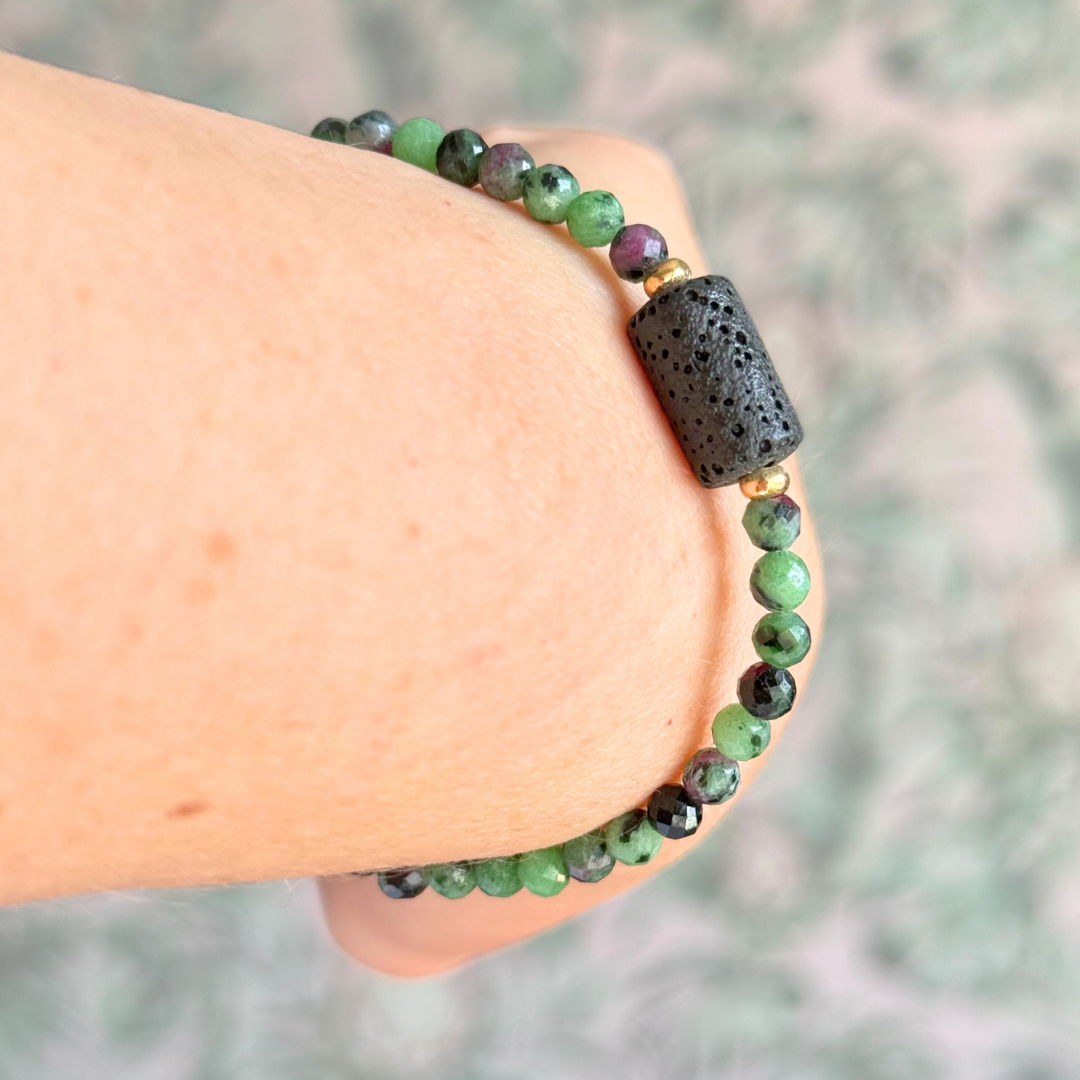 Essential oil diffuser bracelet featuring black lava rock tube bead on the band of 4mm faceted ruby in zoisite beads. Finished with your choice of sterling silver or gold vermeil accent beads.
