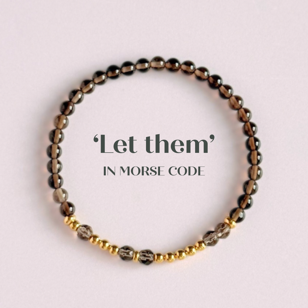 Elasticated smoky quartz crystal morse code bracelet that spells out the words ‘Let them’ in a combination of 4mm round smoky quartz beads, 4mm faceted smoky quartz beads and either sterling silver or gold vermeil 3mm round beads. The words start and end at the rondelle spacer beads.