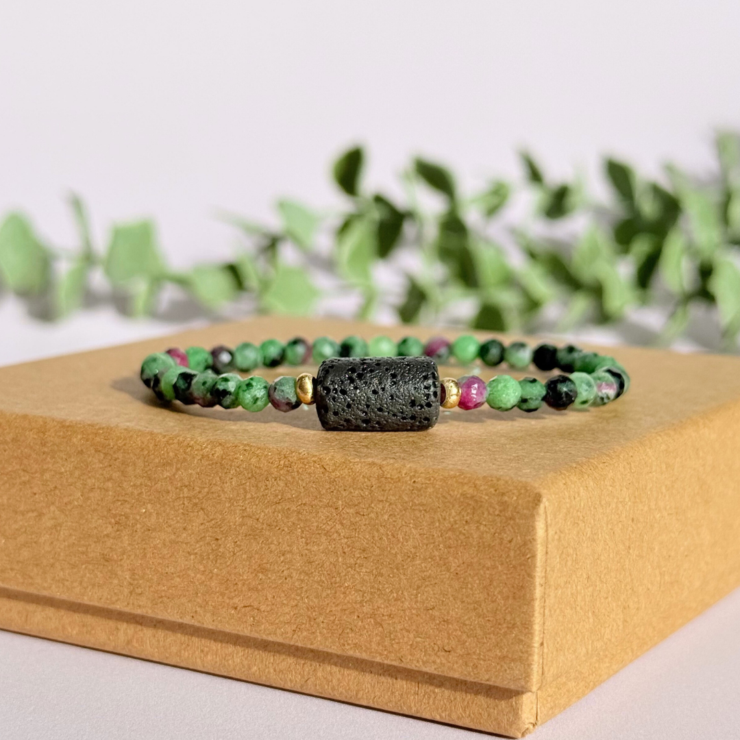 Essential oil diffuser bracelet featuring black lava rock tube bead on the band of 4mm faceted ruby in zoisite beads. Finished with your choice of sterling silver or gold vermeil accent beads.