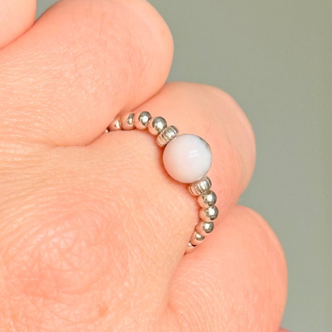 Sterling silver pink opal October birthstone ring featuring a 6mm smooth, round pink opal bead on a band of 2.5mm sterling silver ball beads. Elasticated for comfort.