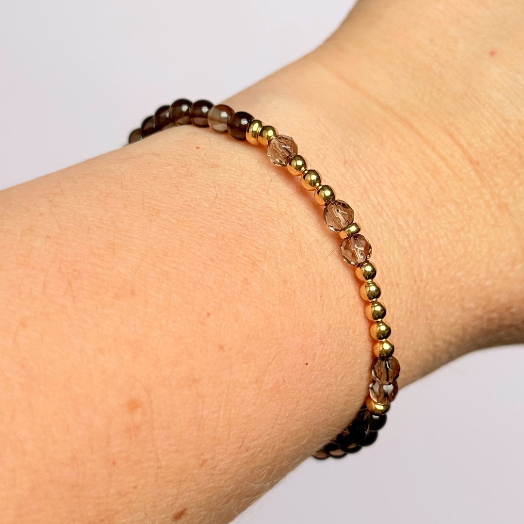 Elasticated smoky quartz crystal morse code bracelet that spells out the words ‘Let them’ in a combination of 4mm round smoky quartz beads, 4mm faceted smoky quartz beads and either sterling silver or gold vermeil 3mm round beads. The words start and end at the rondelle spacer beads.