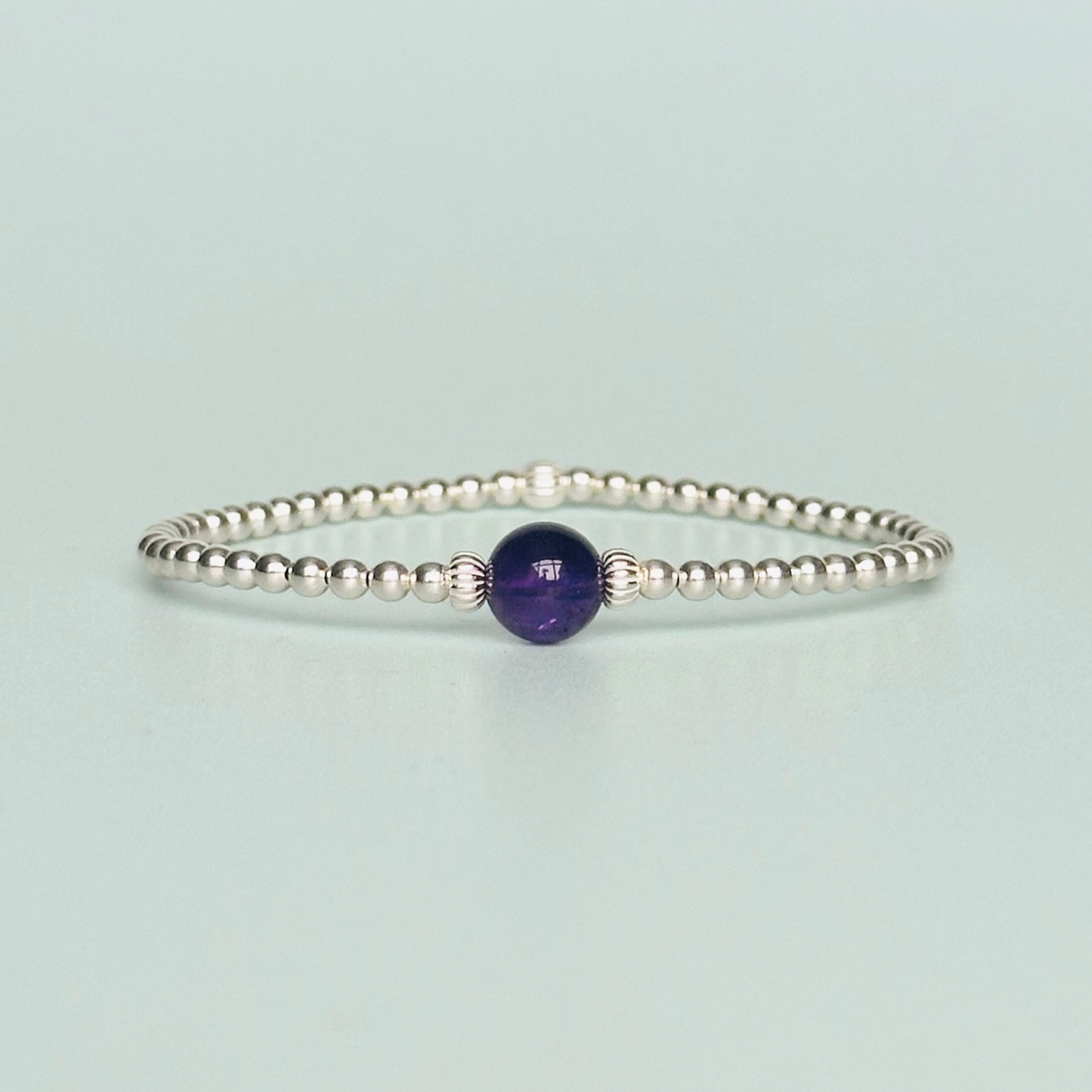 Sterling silver amethyst bracelet features an ethically mined 8mm amethyst bead, flanked by corrugated rondelle beads on a band of 3mm sterling silver beads. A bracelet to promote inner peace and calm.