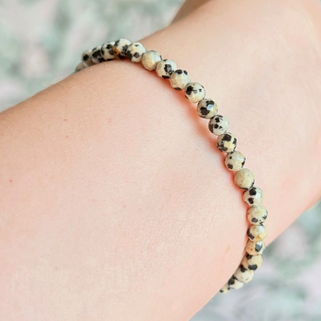 Essential oil diffuser bracelet featuring black lava rock tube bead on the band of 4mm faceted dalmatian jasper beads. Finished with your choice of sterling silver or gold vermeil accent beads.