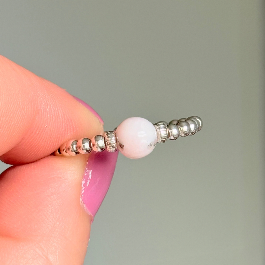 Sterling silver pink opal October birthstone ring featuring a 6mm smooth, round pink opal bead on a band of 2.5mm sterling silver ball beads. Elasticated for comfort.