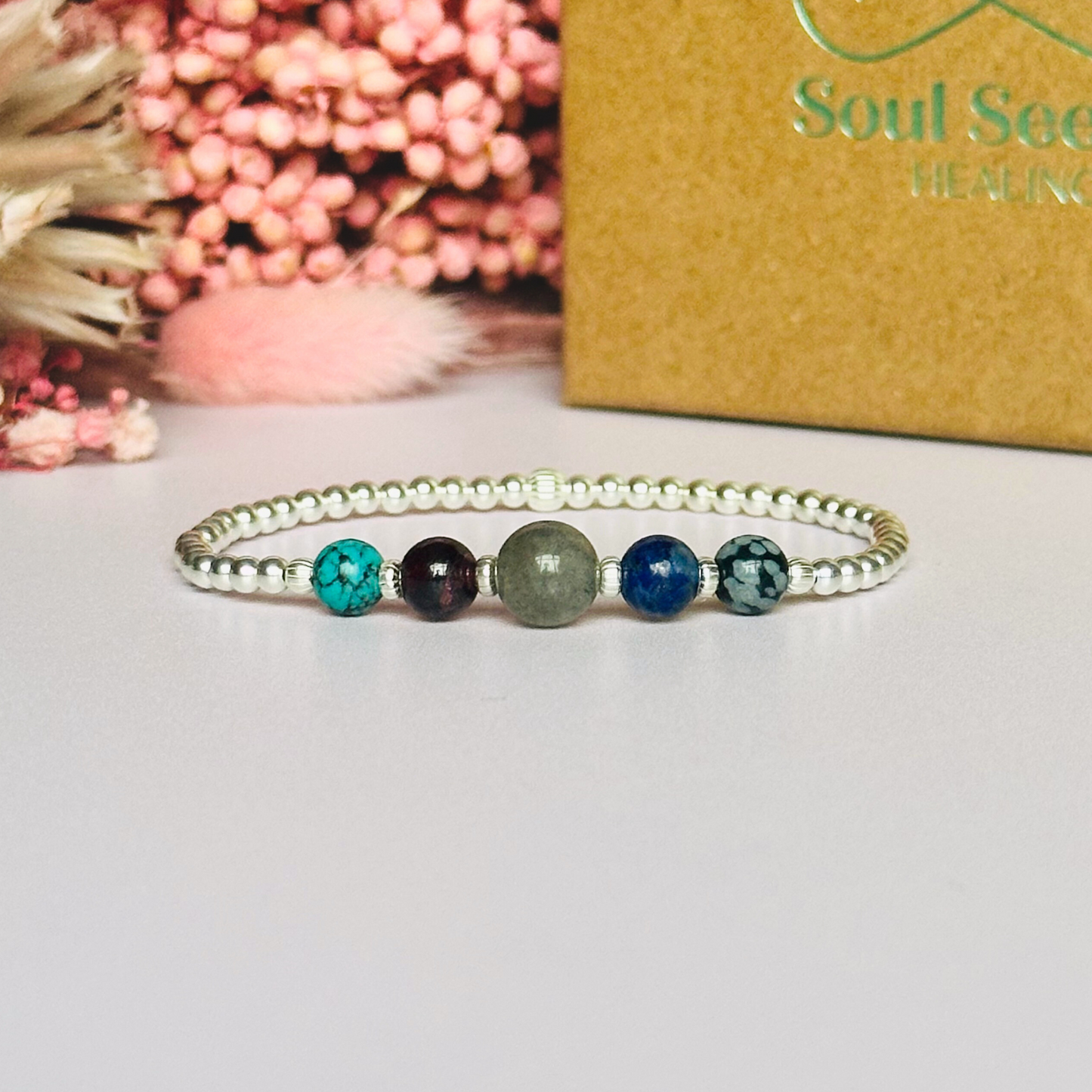 This sterling silver Sagittarius bracelet is made with a selection of five healing crystals all believed to resonate with the Sagittarius zodiac sign. The central bead is 8mm, the other four are 6mm. On an elasticated band of 3mm sterling silver beads with corrugated accent beads. Featuring garnet, labradorite, lapis lazuli, snowflake obsidian and turquoise.