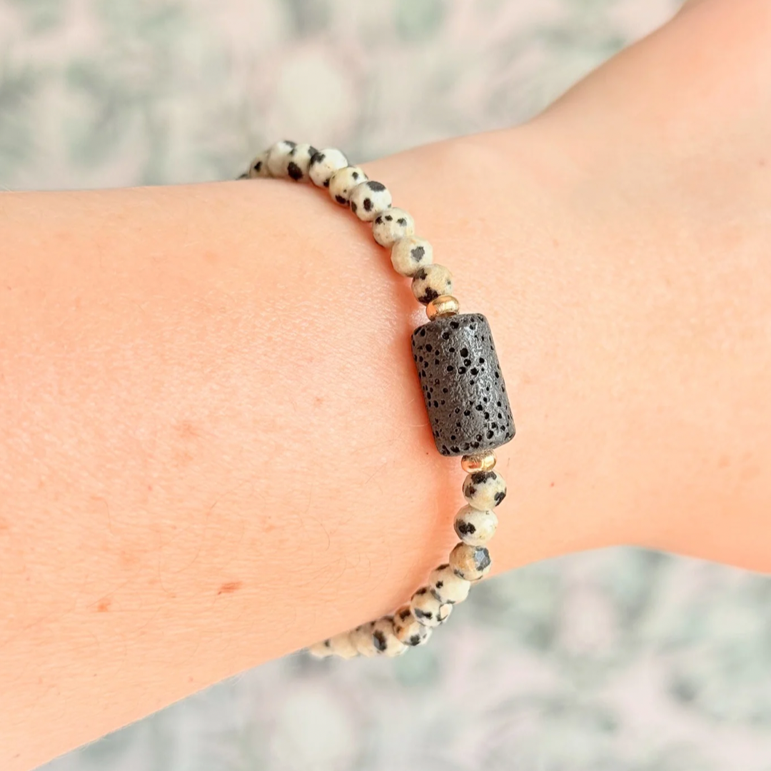 Essential oil diffuser bracelet featuring black lava rock tube bead on the band of 4mm faceted dalmatian jasper beads. Finished with your choice of sterling silver or gold vermeil accent beads.