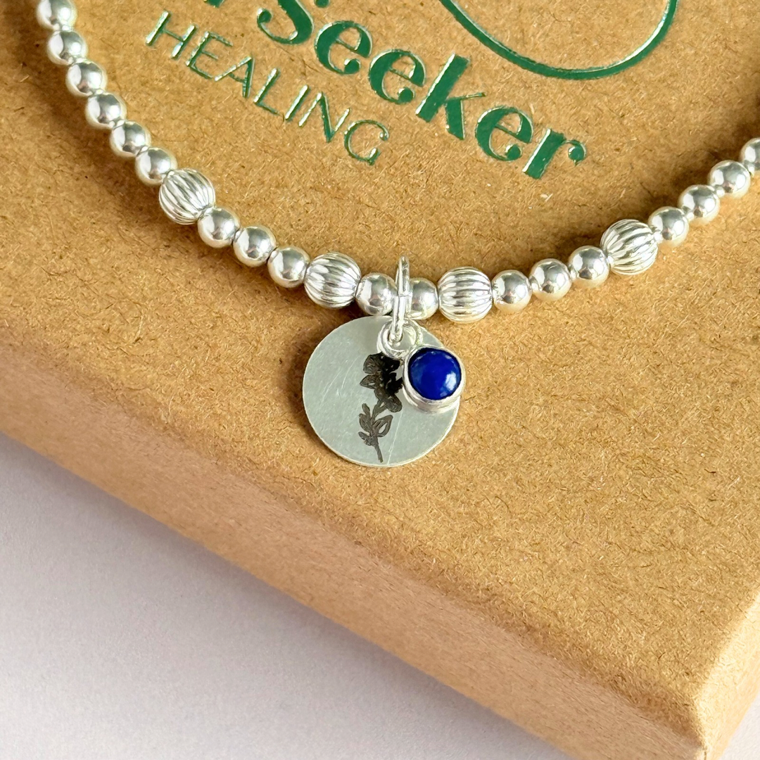 This sterling silver bracelet features a domed 4mm lapis lazuli cabochon charm, the birth stone for September, in a sterling silver setting. It features an 11mm sterling silver disc charm, which is engraved with the September birth flower, Morning Glory. This charm can be personalised on one side if required or feature the same flower graphic on both sides. The main band of the bracelet is made up of 3 mm sterling silver round ball beads with some corrugated accent beads.