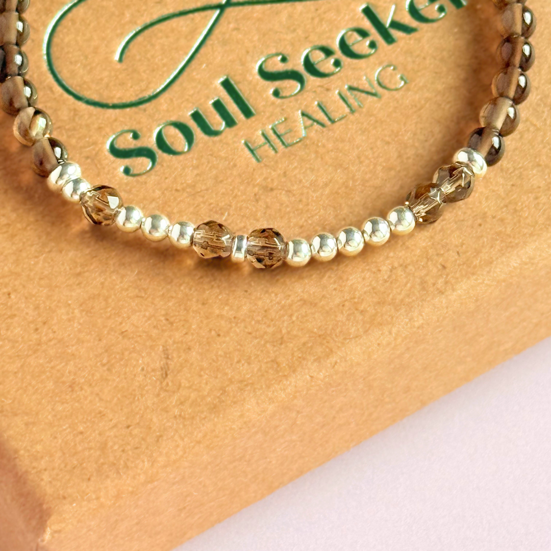 Elasticated smoky quartz crystal morse code bracelet that spells out the words ‘Let them’ in a combination of 4mm round smoky quartz beads, 4mm faceted smoky quartz beads and either sterling silver or gold vermeil 3mm round beads. The words start and end at the rondelle spacer beads.