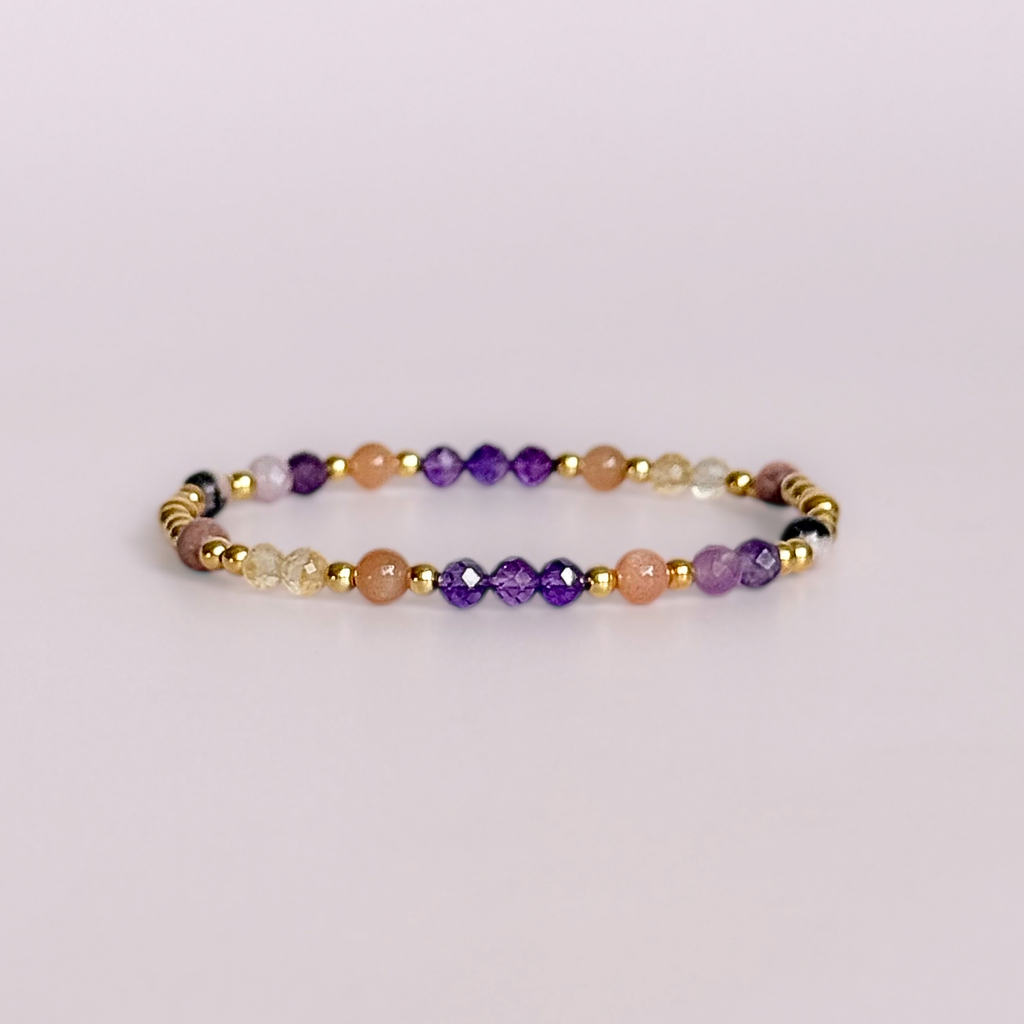 Dainty gold vermeil crystal bracelet featuring five crystals, in 4mm faceted and smooth round style, each believed to help with menopause symptoms. Featuring amethyst, citrine, lepidolite, peach moonstone and pink zebra jasper. Pictured against a light pink background.