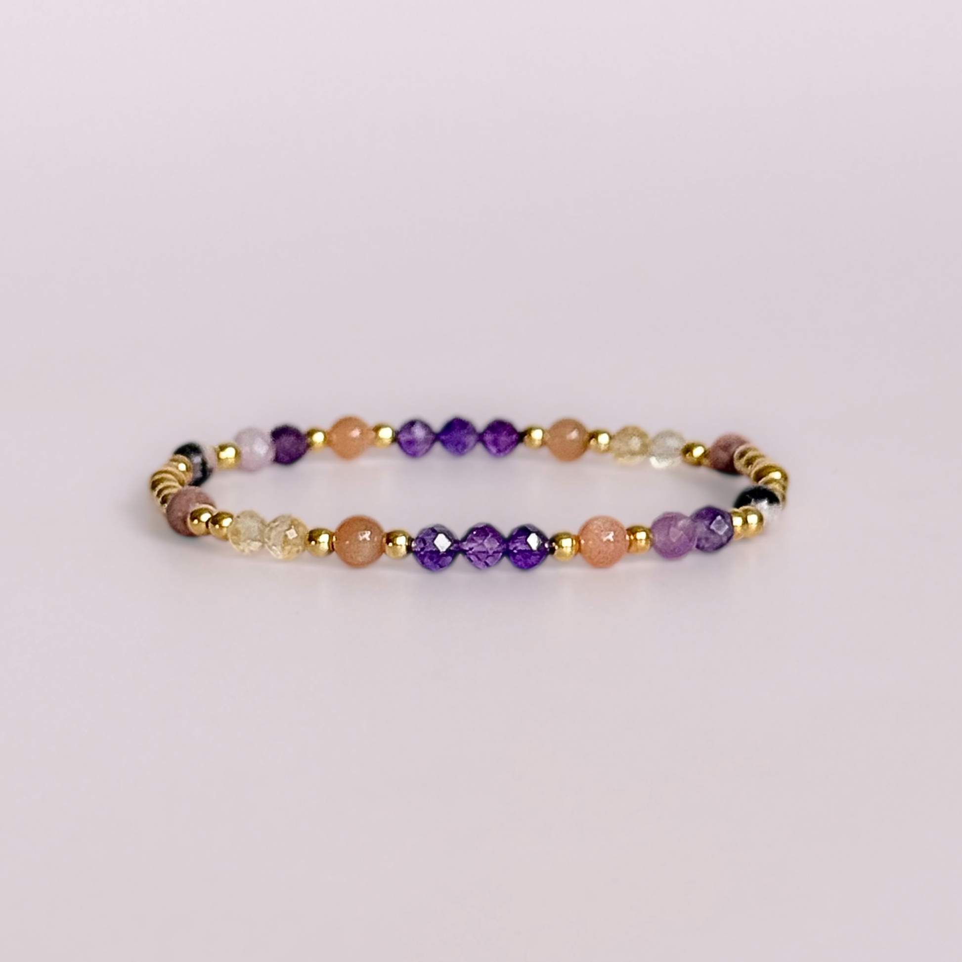 Dainty gold vermeil crystal bracelet featuring five crystals, in 4mm faceted and smooth round style, each believed to help with menopause symptoms. Featuring amethyst, citrine, lepidolite, peach moonstone and pink zebra jasper. Pictured against a light pink background.