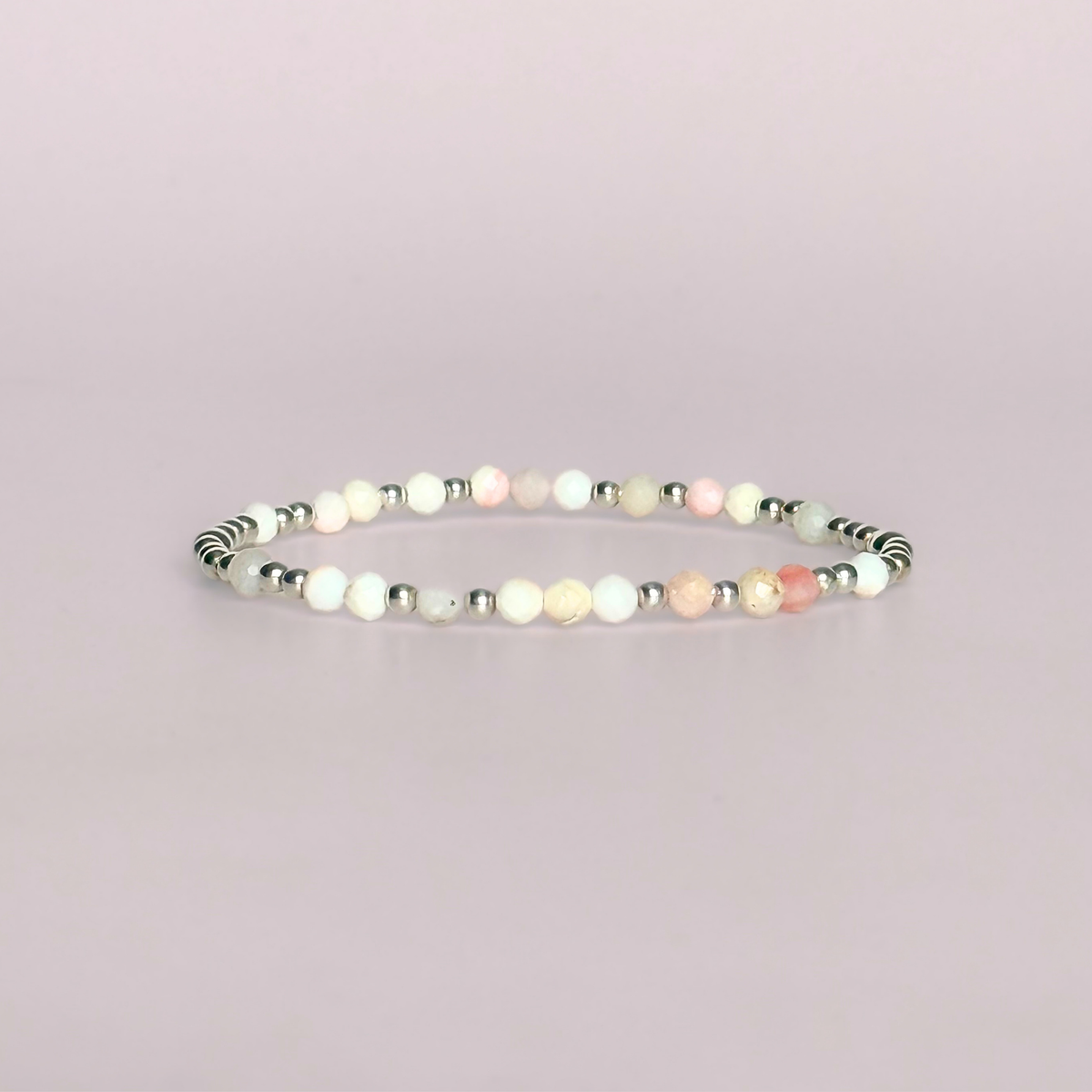Dainty, minimalist sterling silver and pink opal October birthstone stacking bracelet. Made with 4mm faceted pink opal beads and 3mm sterling silver round beads. Elasticated for comfort. Pictured against a light pink background