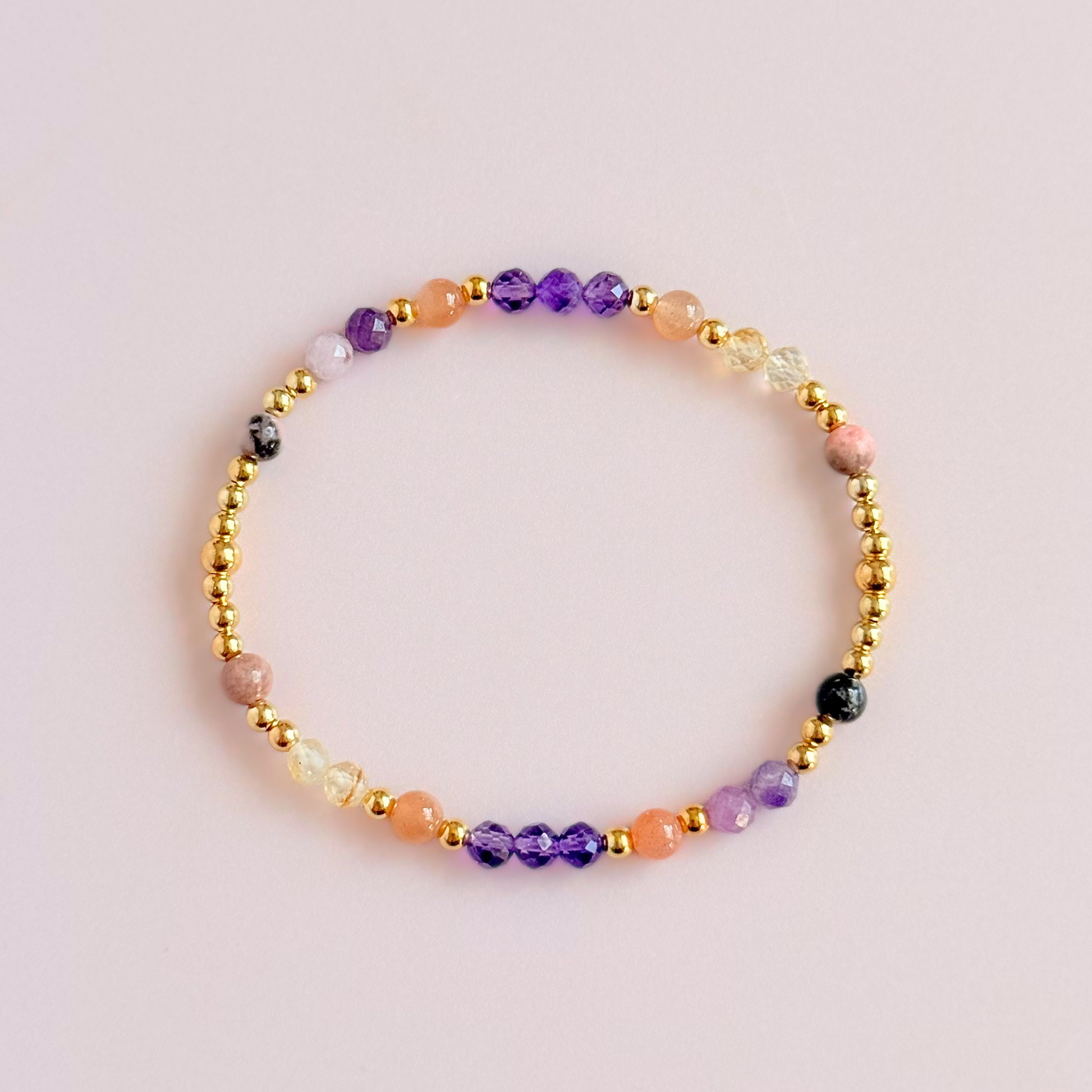 Dainty gold vermeil crystal bracelet featuring five crystals, in 4mm faceted and smooth round style, each believed to help with menopause symptoms. Featuring amethyst, citrine, lepidolite, peach moonstone and pink zebra jasper. Pictured from above, against a light pink background.