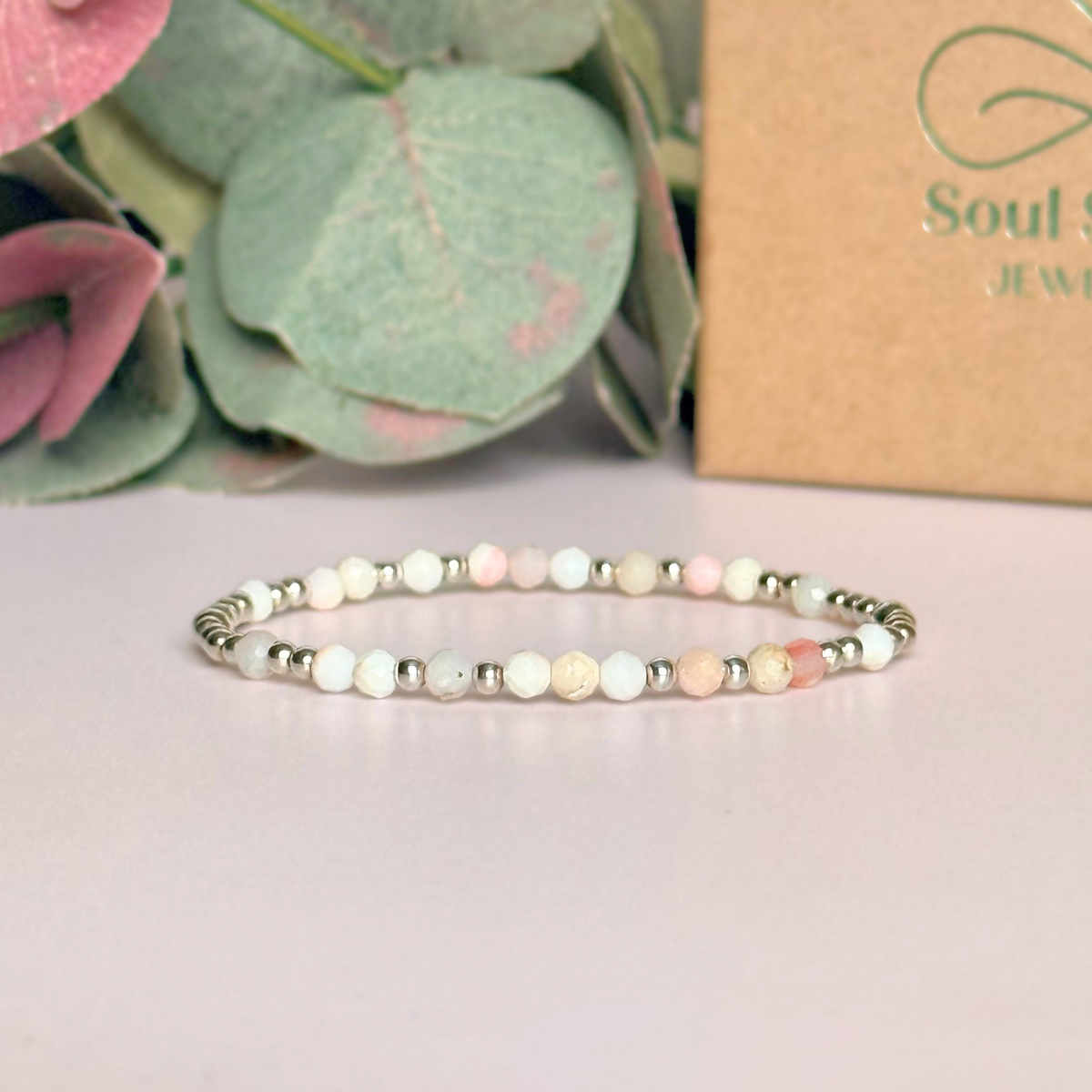 Dainty, minimalist sterling silver and pink opal October birthstone stacking bracelet. Made with 4mm faceted pink opal beads and 3mm sterling silver round beads. Elasticated for comfort. Pictured in front of the gift box