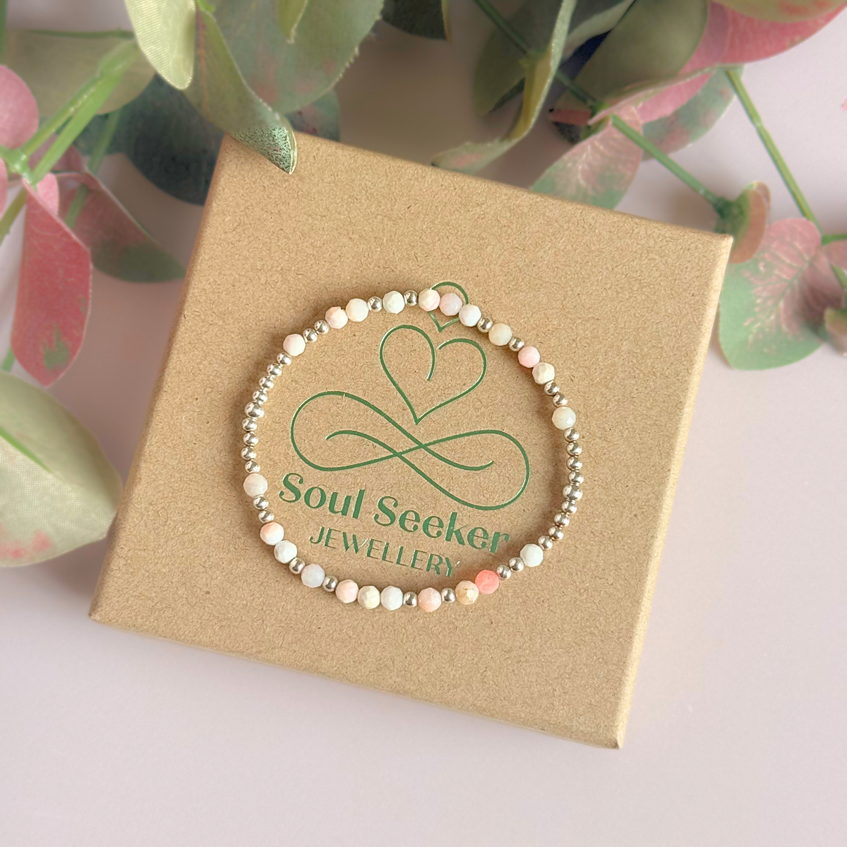 Dainty, minimalist sterling silver and pink opal October birthstone stacking bracelet. Made with 4mm faceted pink opal beads and 3mm sterling silver round beads. Elasticated for comfort. Pictured on top of the gift box
