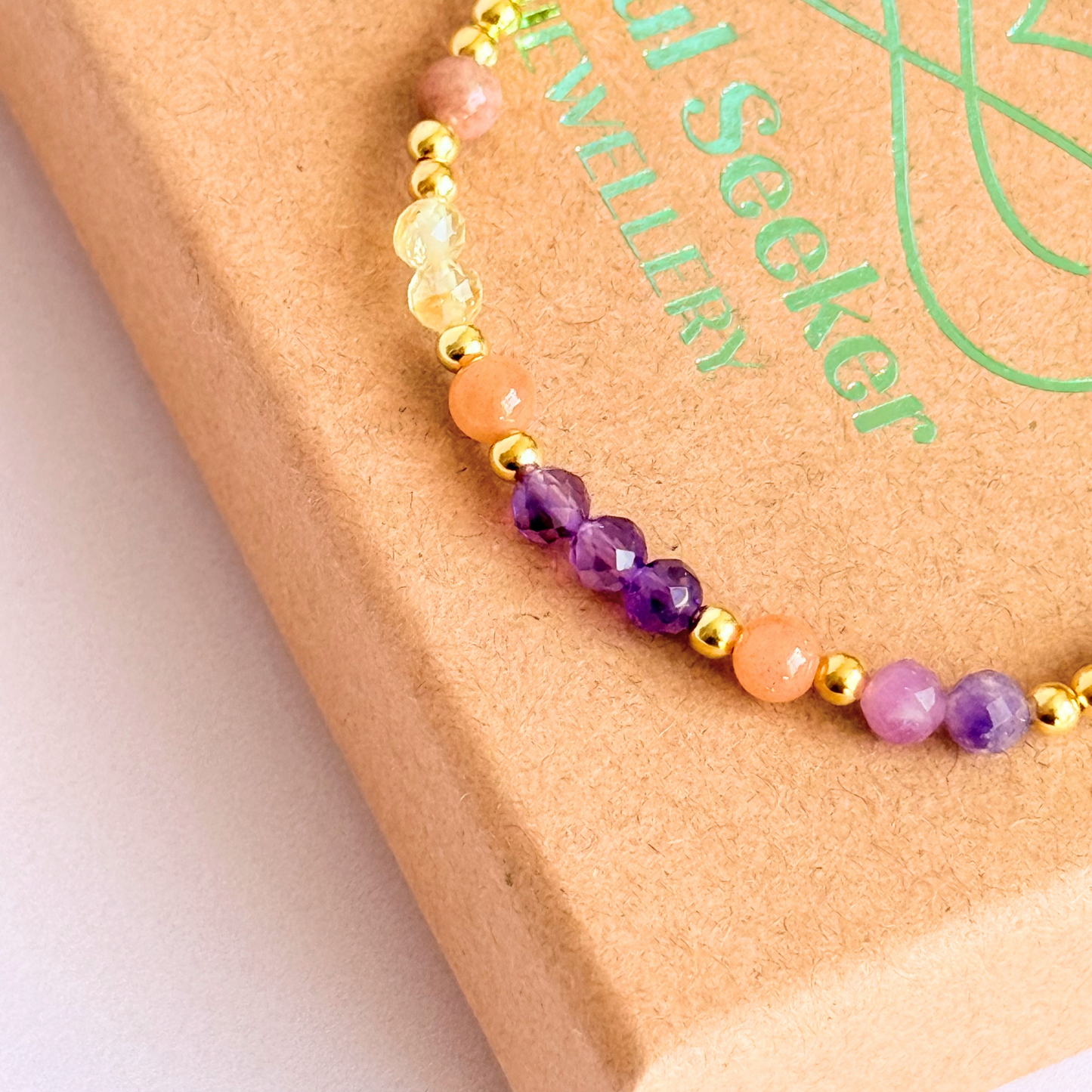 Dainty gold vermeil crystal bracelet featuring five crystals, in 4mm faceted and smooth round style, each believed to help with menopause symptoms. Featuring amethyst, citrine, lepidolite, peach moonstone and pink zebra jasper. Pictured on top of gift box, close up.