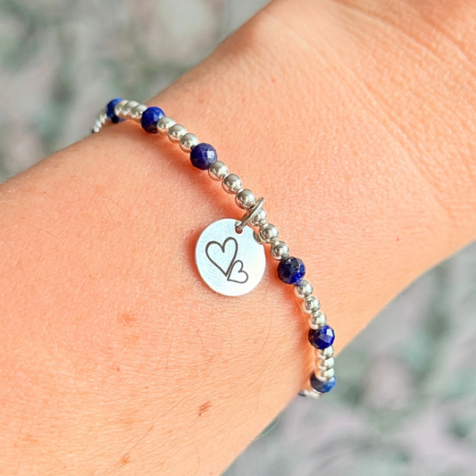 Sterling silver bracelet features 4mm lapis lazuli faceted beads, separated by 3mm sterling silver round beads. Lapis lazuli is a September birthstone. The focal point is an 11mm sterling silver charm, engraved with a large and smaller heart design. This charm can be personalised on one side if required or feature the same graphic on both sides.