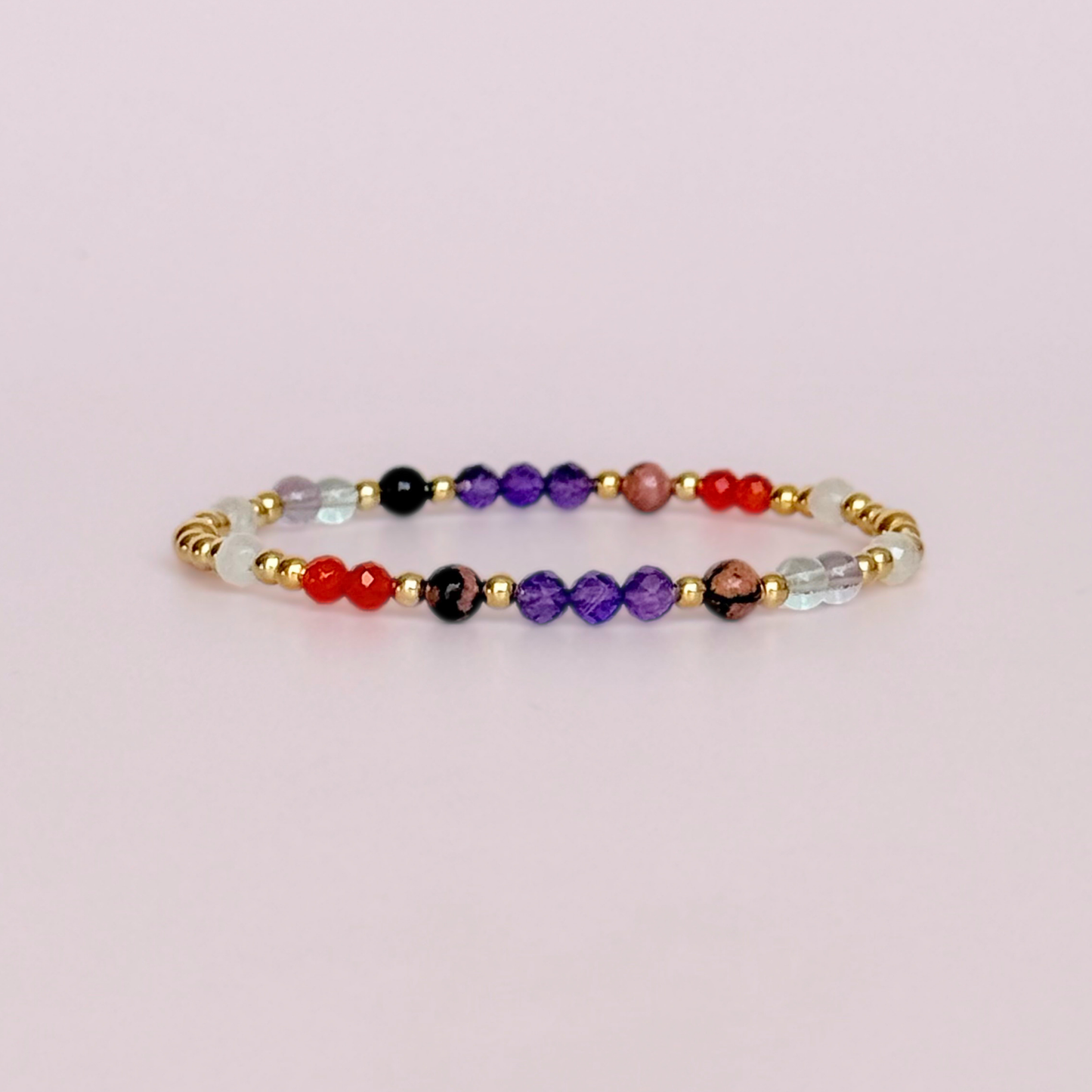 Dainty gold vermeil crystal bracelet featuring five crystals, in 4mm faceted and smooth round style, each believed to help with perimenopause symptoms. Featuring amethyst, rhodonite, fluorite, moonstone and carnelian. Pictured against a light pink background.