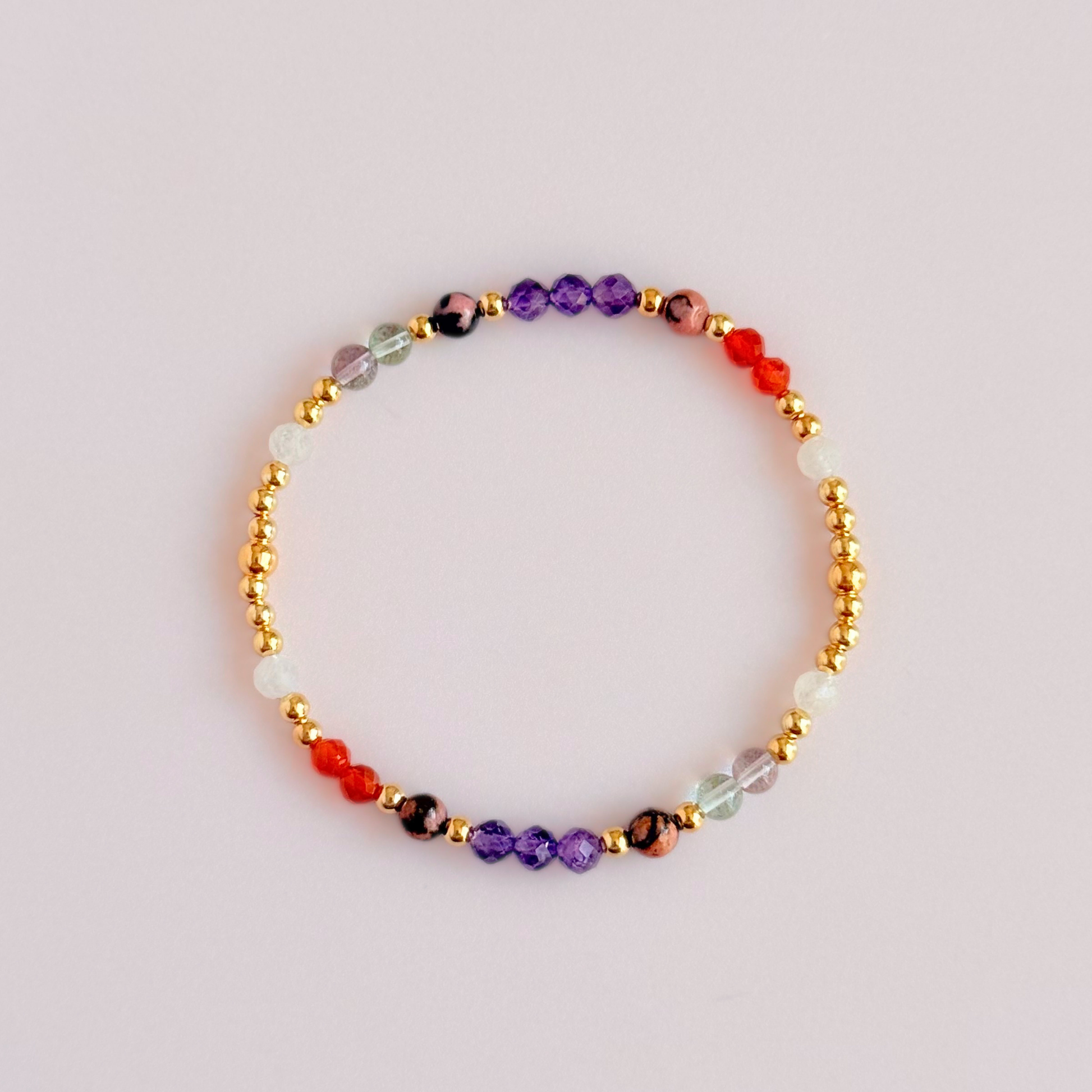 Dainty gold vermeil crystal bracelet featuring five crystals, in 4mm faceted and smooth round style, each believed to help with perimenopause symptoms. Featuring amethyst, rhodonite, fluorite, moonstone and carnelian. Pictured from above, against a light pink background.