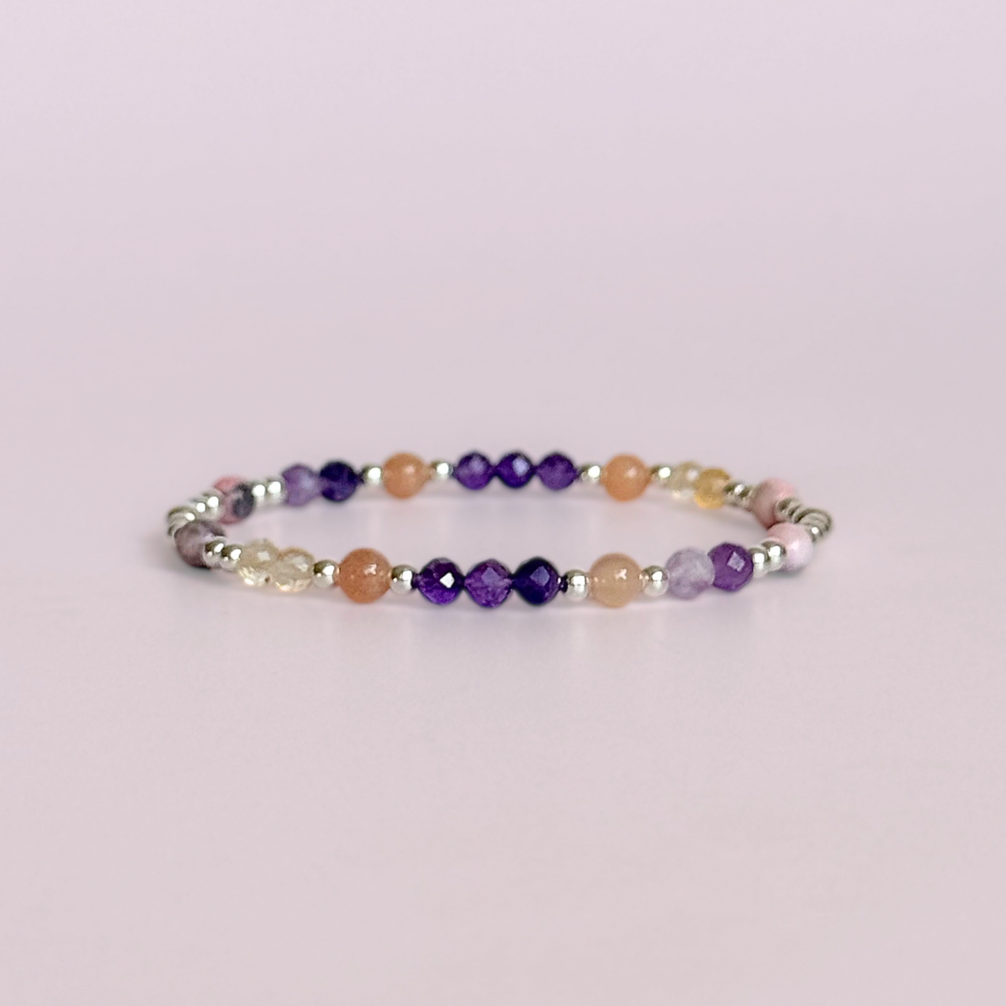 Dainty sterling silver crystal bracelet featuring five crystals, in 4mm faceted and smooth round style, each believed to help with menopause symptoms. Featuring amethyst, citrine, lepidolite, peach moonstone and pink zebra jasper. Pictured against a light pink background.