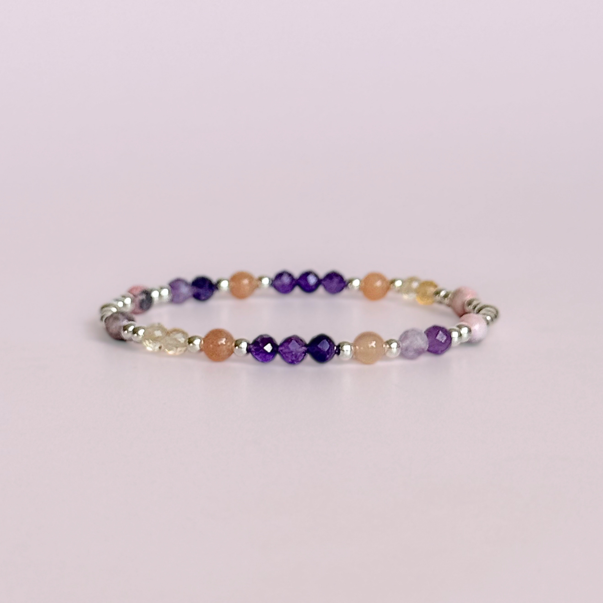 Dainty sterling silver crystal bracelet featuring five crystals, in 4mm faceted and smooth round style, each believed to help with menopause symptoms. Featuring amethyst, citrine, lepidolite, peach moonstone and pink zebra jasper. Pictured against a light pink background.