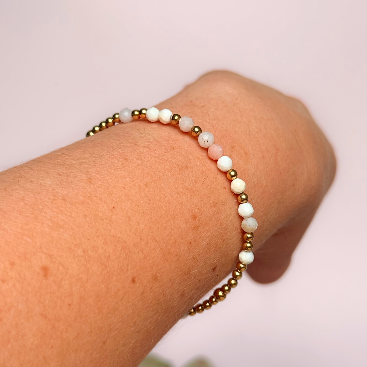 Dainty, minimalist gold vermeil and pink opal October birthstone stacking bracelet. Made with 4mm faceted pink opal beads and 3mm gold vermeil round beads. Elasticated for comfort. Pictured being worn, on an angle
