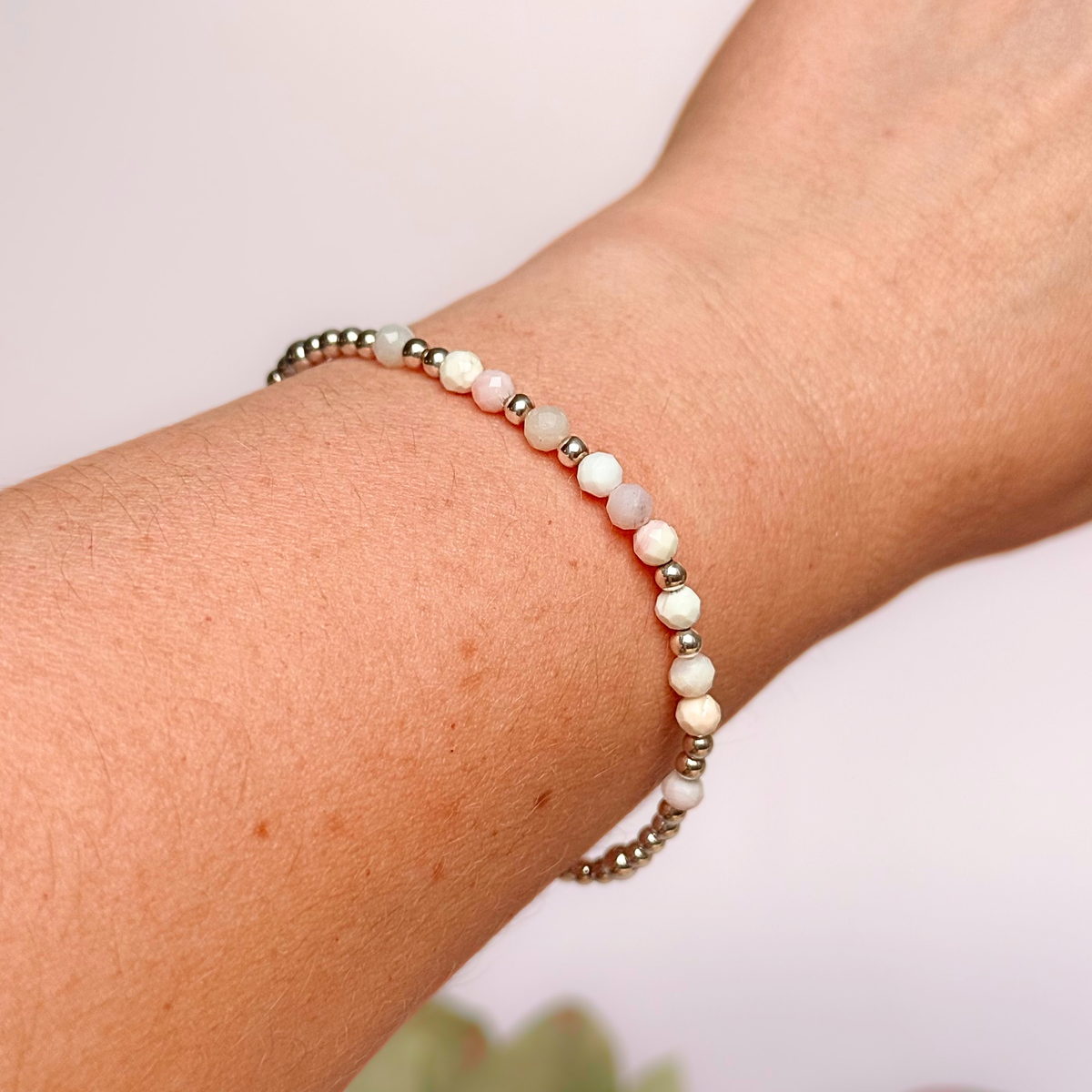 Dainty, minimalist sterling silver and pink opal October birthstone stacking bracelet. Made with 4mm faceted pink opal beads and 3mm sterling silver round beads. Elasticated for comfort. Pictured being worn