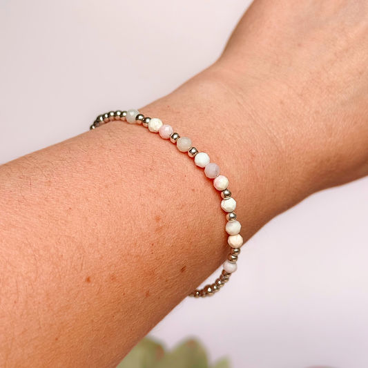 Dainty, minimalist sterling silver and pink opal October birthstone stacking bracelet. Made with 4mm faceted pink opal beads and 3mm sterling silver round beads. Elasticated for comfort. Pictured being worn
