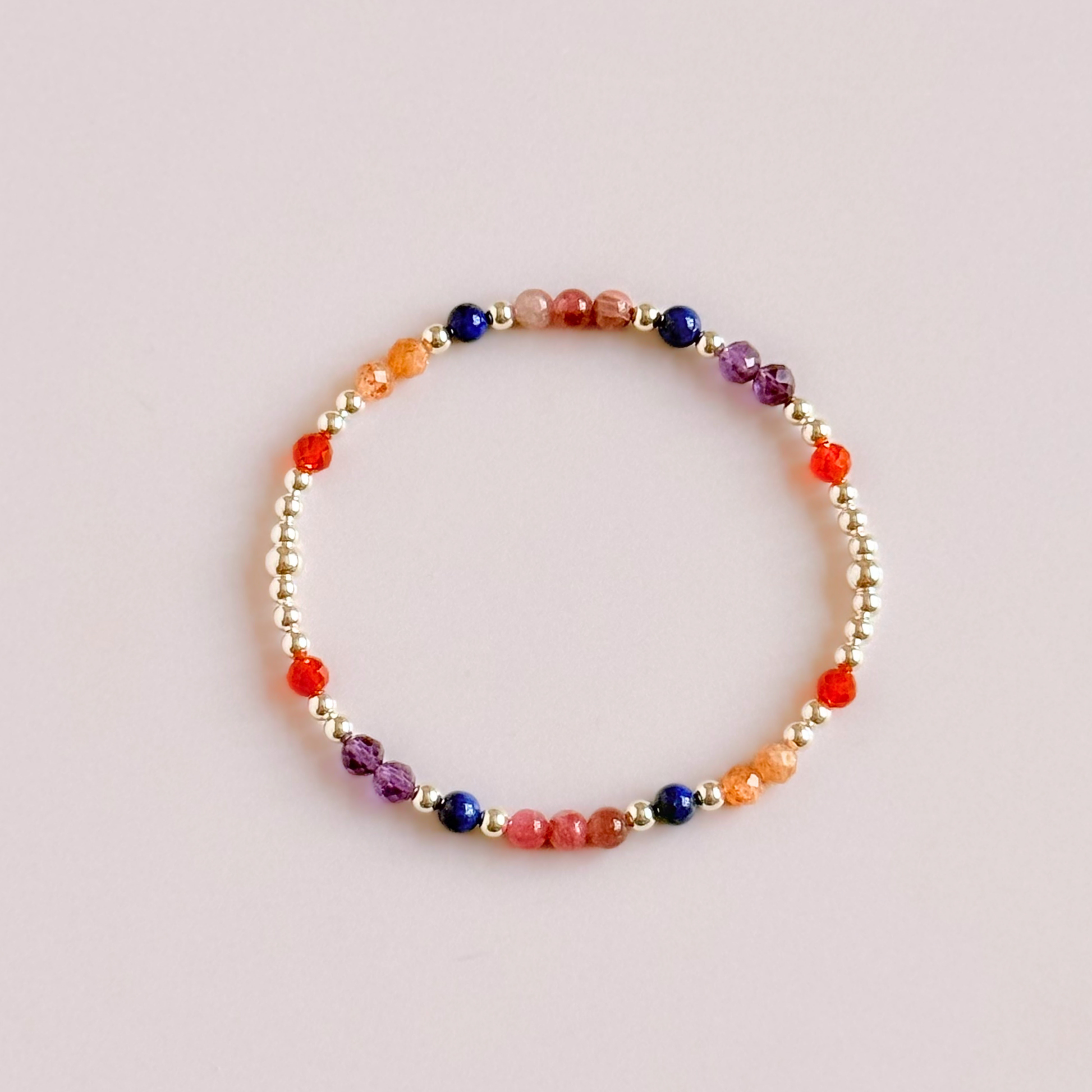 ‘Arabian Sunset' sterling silver dainty beaded bracelet with pink tourmaline, sunstone, carnelian, lapis lazuli and amethyst. Made with round 3mm sterling silver beads and 4mm smooth and faceted round crystal gemstone beads. Pictured from above, against a pink background