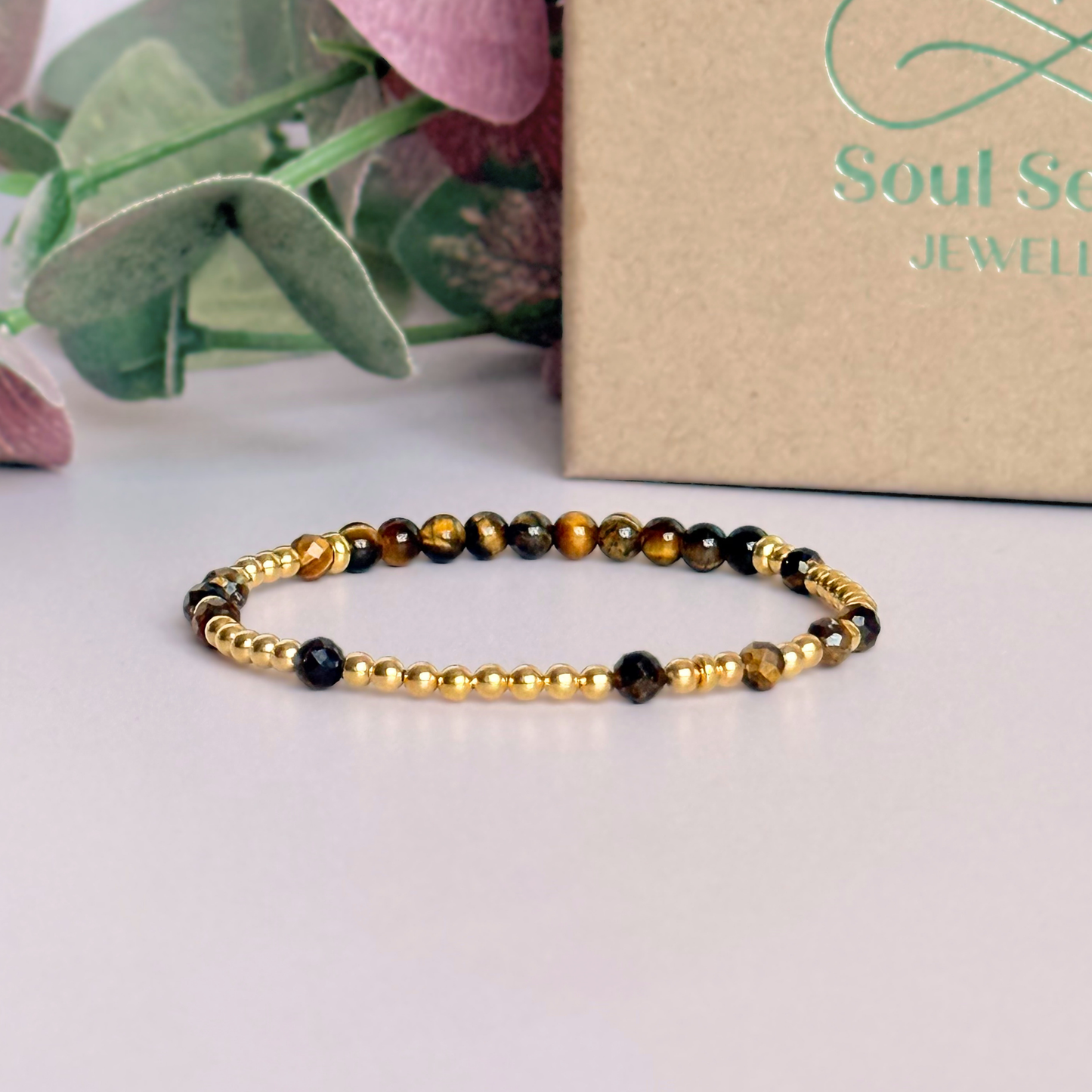 Tigers eye morse code bracelet that spells out the words ‘Ask, believe, receive’ in a combination of 4mm round smooth and faceted crystal beads with your choice of sterling silver or gold vermeil accent beads. Pictured in gold, in front of the gift box