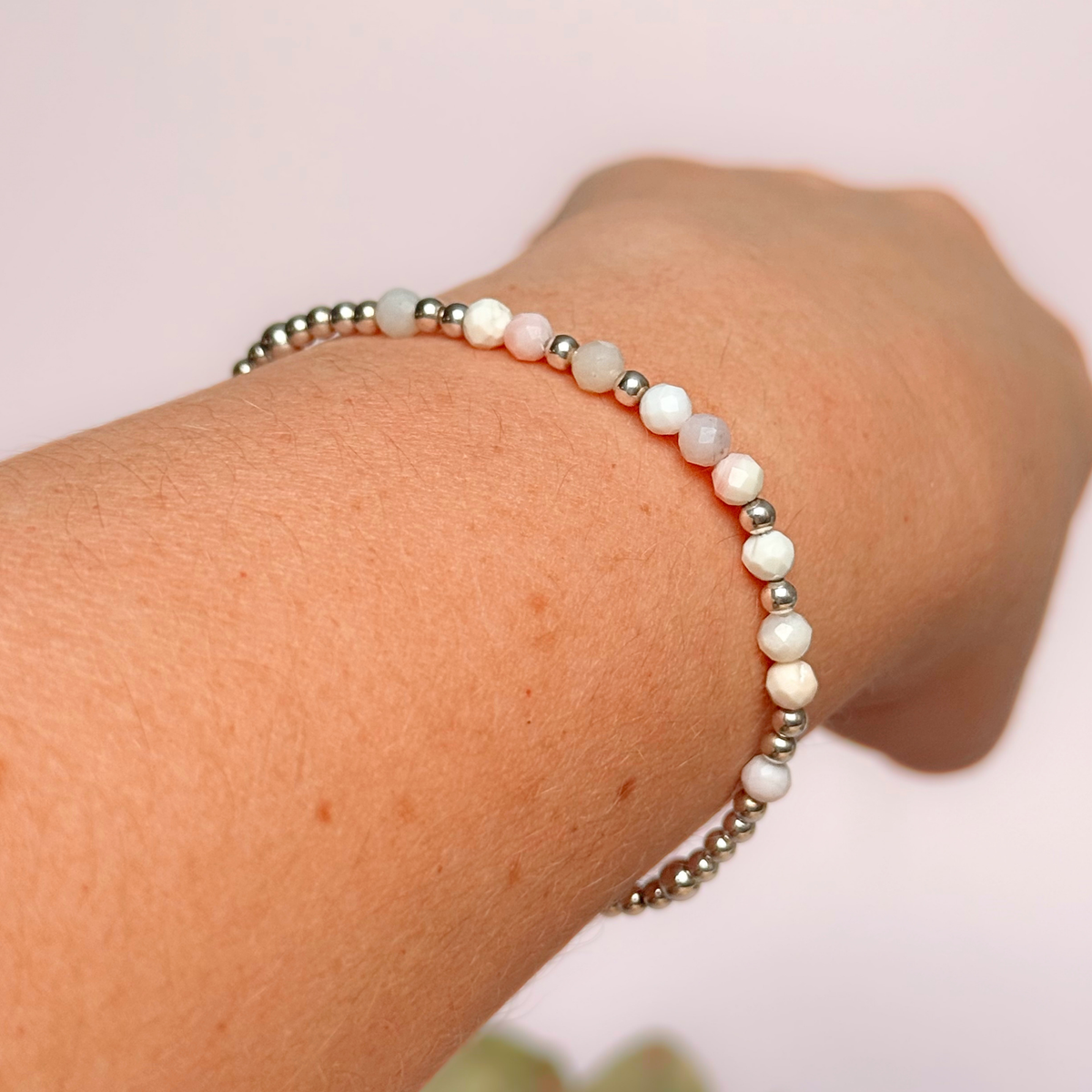 Dainty, minimalist sterling silver and pink opal October birthstone stacking bracelet. Made with 4mm faceted pink opal beads and 3mm sterling silver round beads. Elasticated for comfort. Pictured being worn, at an angle