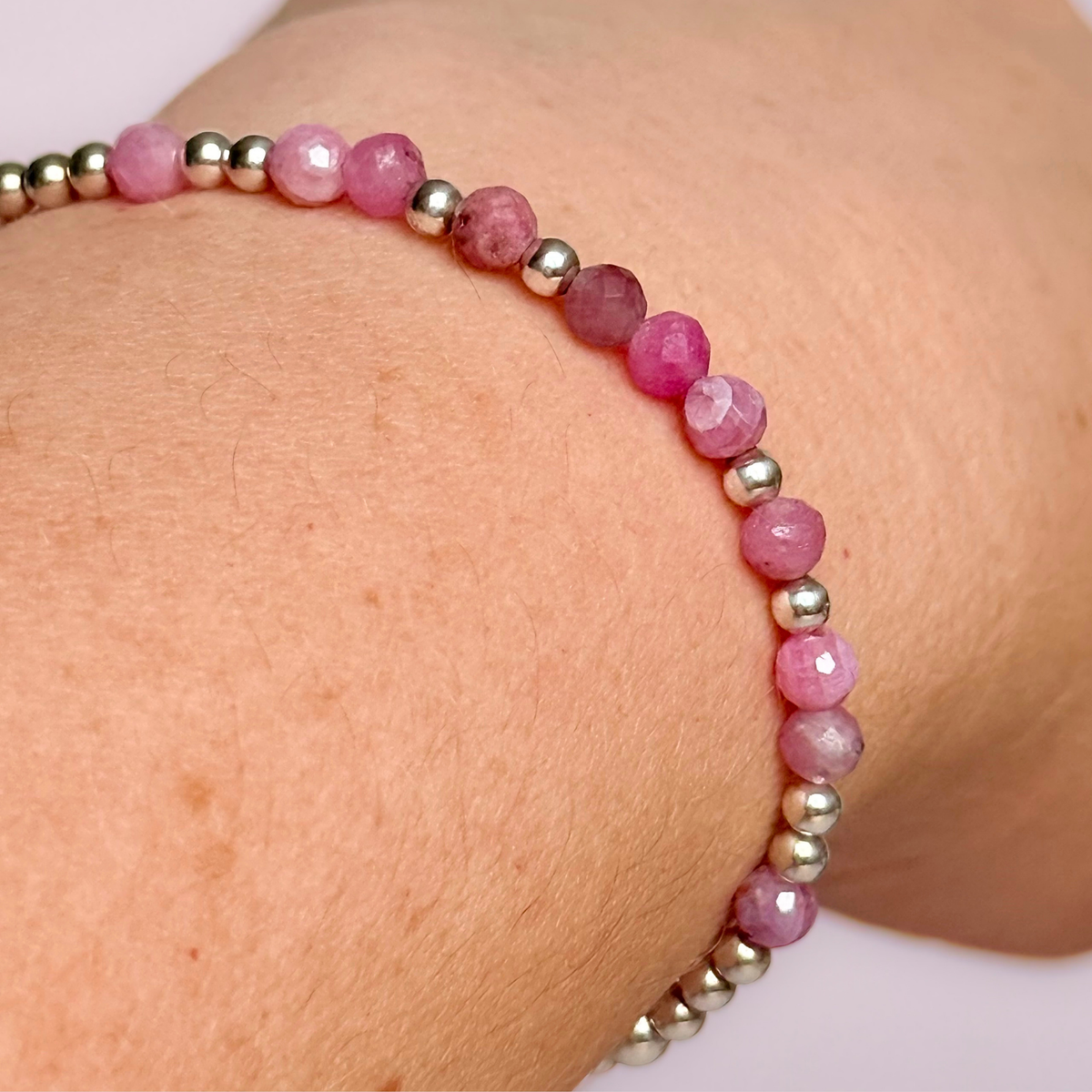 Dainty, minimalist sterling silver and pink tourmaline October birthstone stacking bracelet. Made with 4mm faceted pink tourmaline beads and 3mm sterling silver round beads. Elasticated for comfort. Pictured being worn, close up